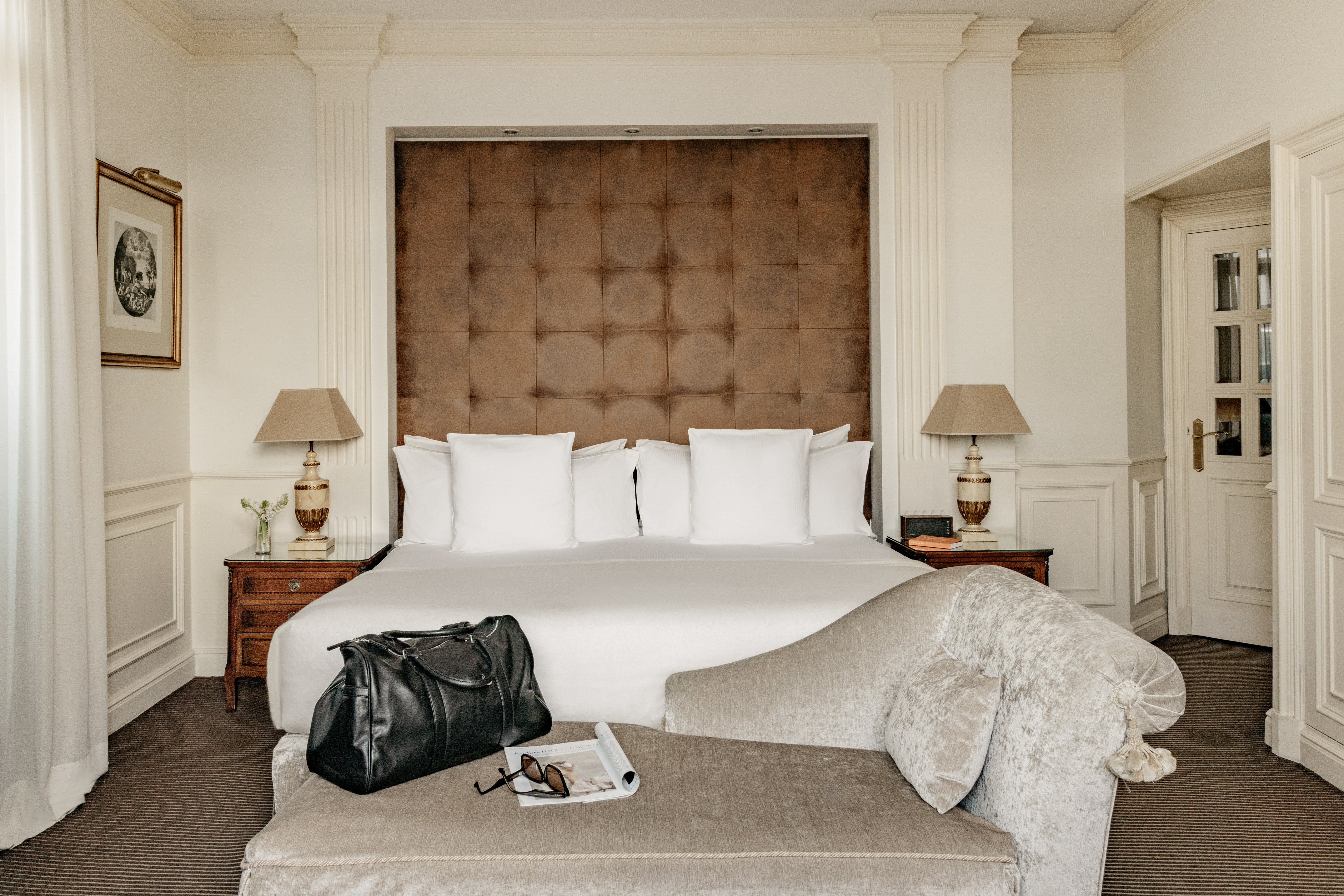 Stylish hotel bedroom with large bed, brown tufted headboard, and travel bag.