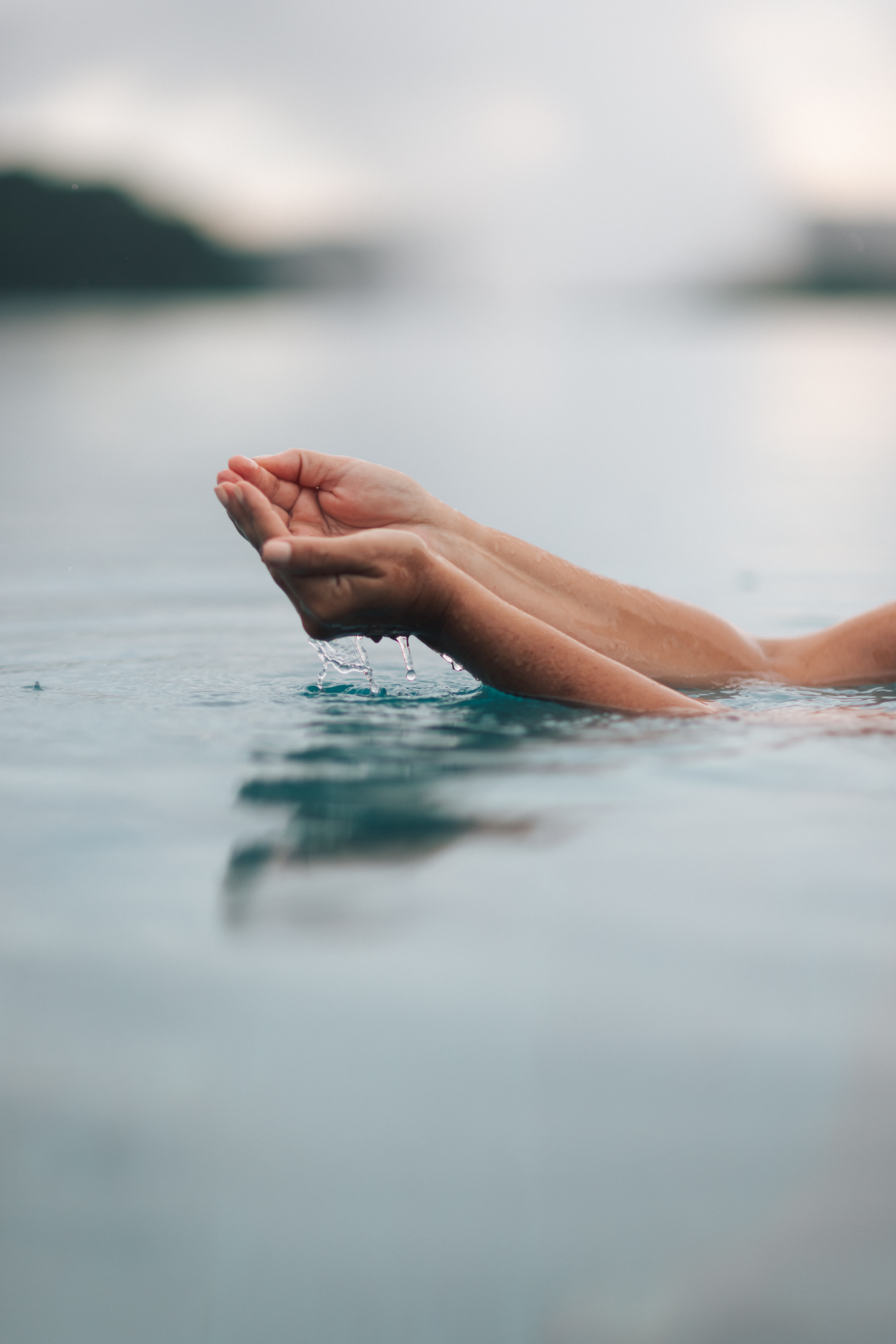 Cupped hands in blue water, drops falling. Refreshing natural scene.