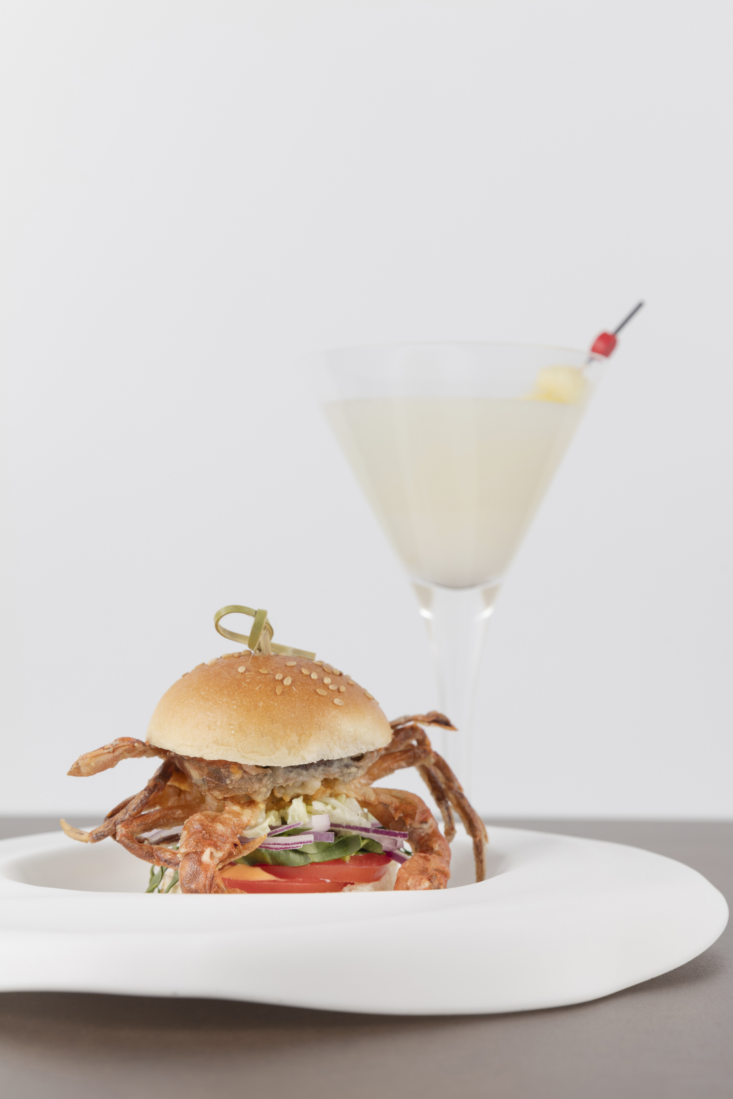 Fried soft-shell crab burger with fresh vegetables, served with a cocktail.