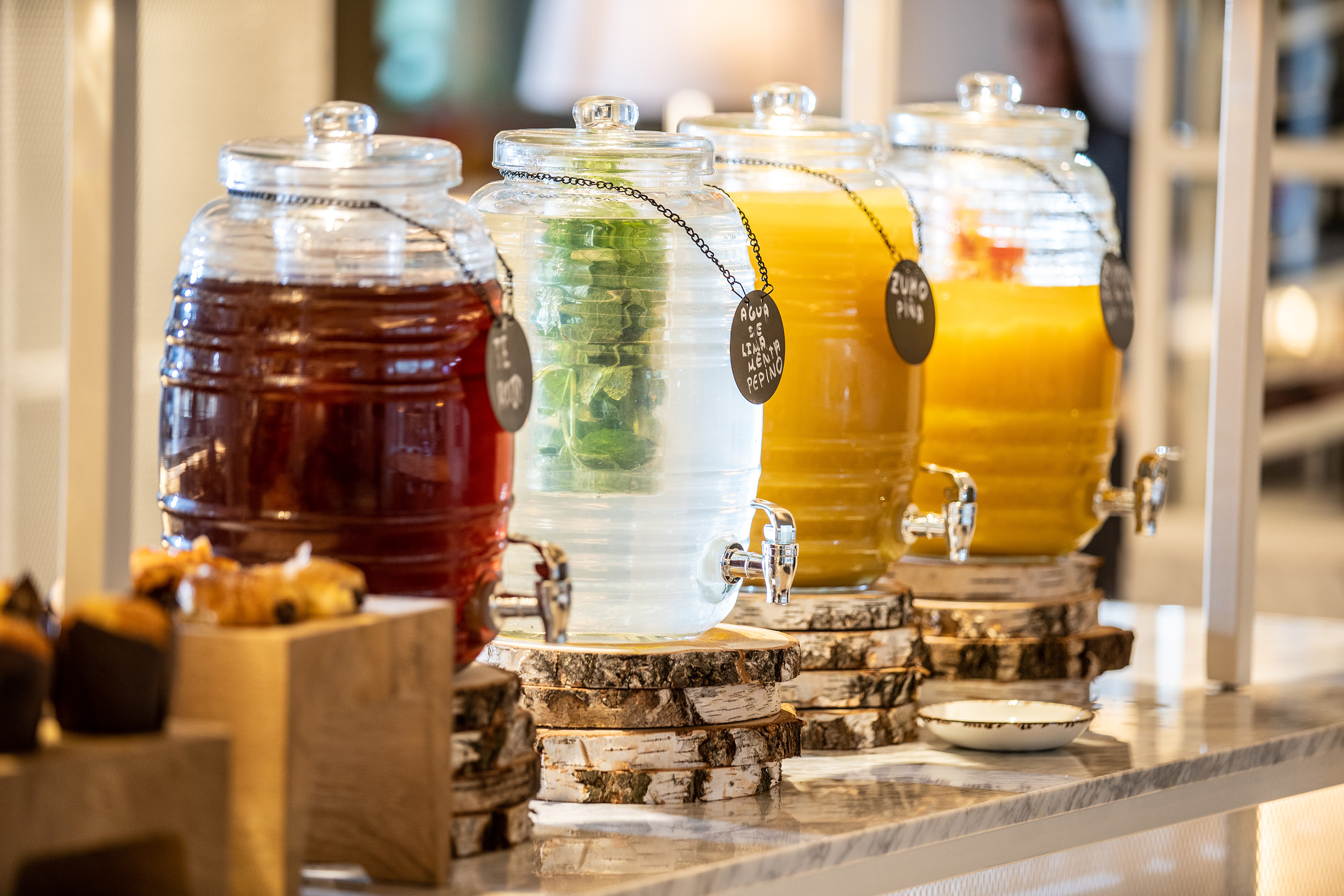 Buffet with four beverage dispensers: tea, infused water, and fruit juices.
