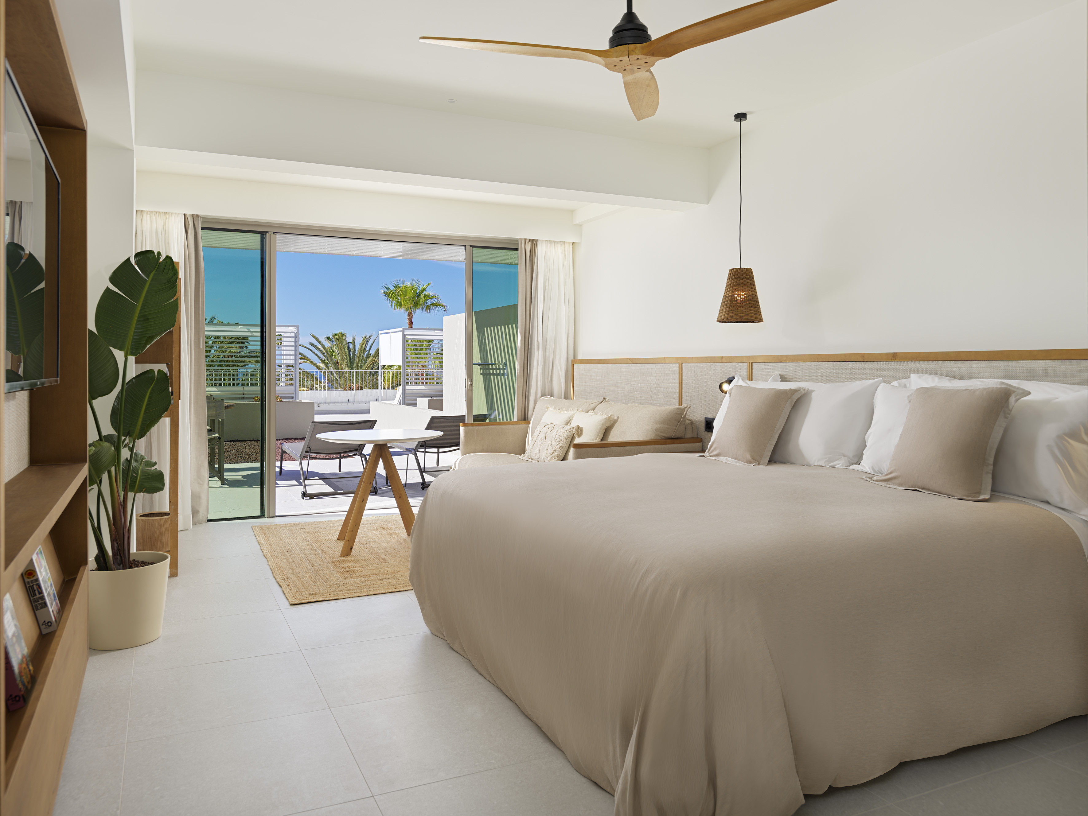 Bright hotel suite with balcony, king bed, ceiling fan, and tropical views.