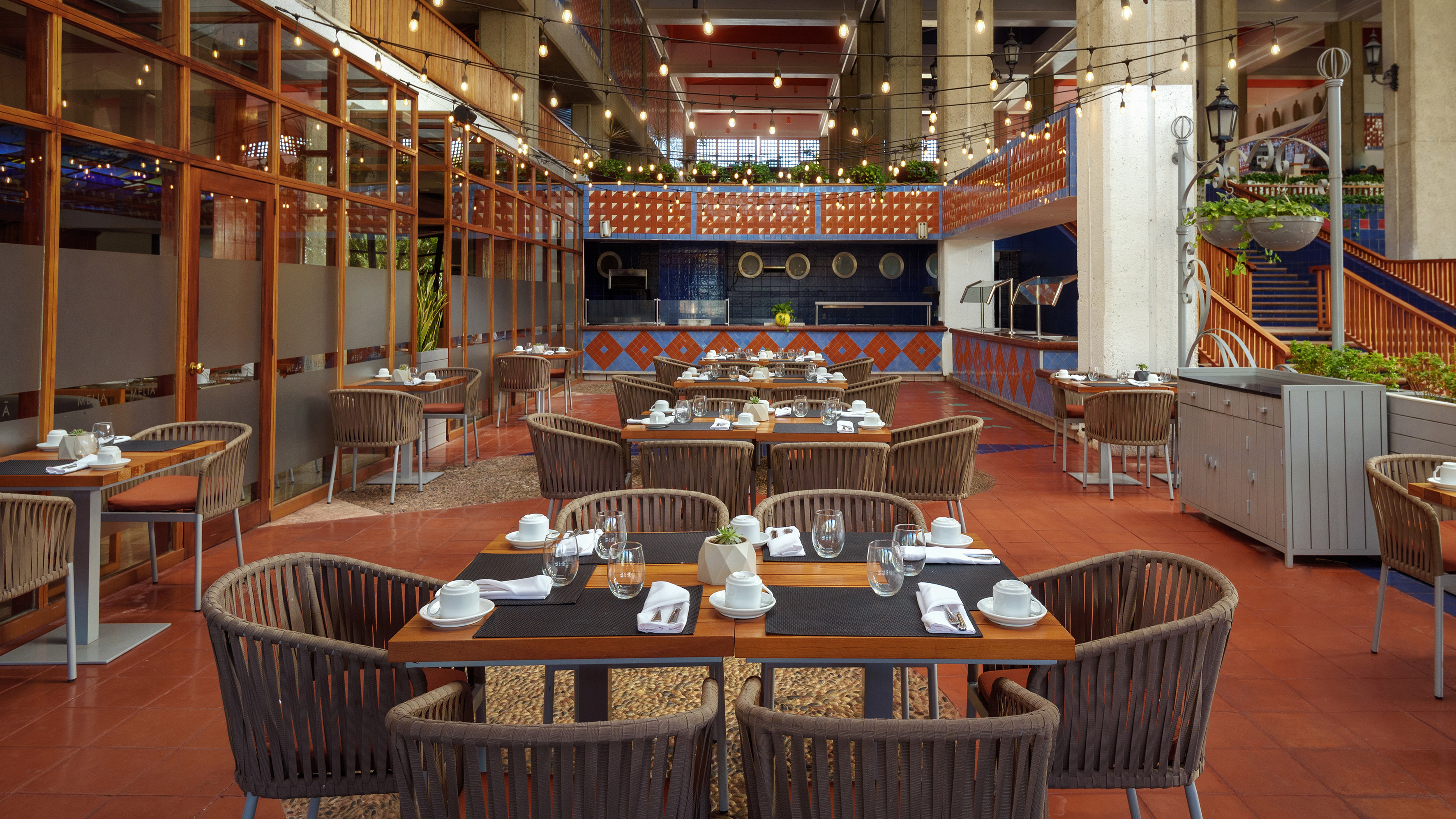 Spacious hotel restaurant dining area with set tables, buffet, and string lights.