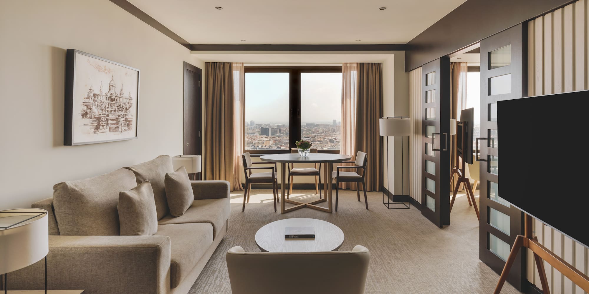 Suite de lujo con sala, sofá, mesa de comedor y vistas panorámicas a la ciudad.