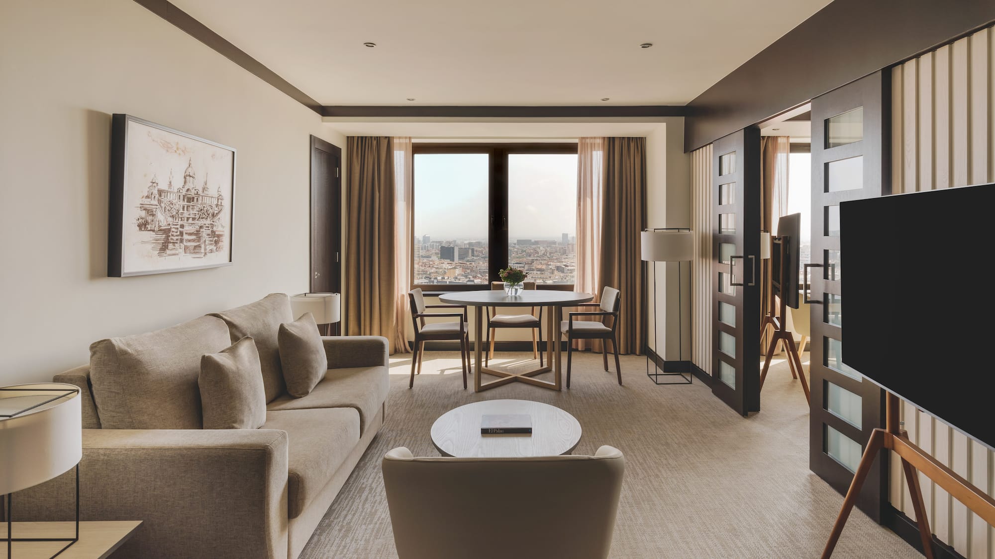 Suite de lujo con sala, sofá, mesa de comedor y vistas panorámicas a la ciudad.