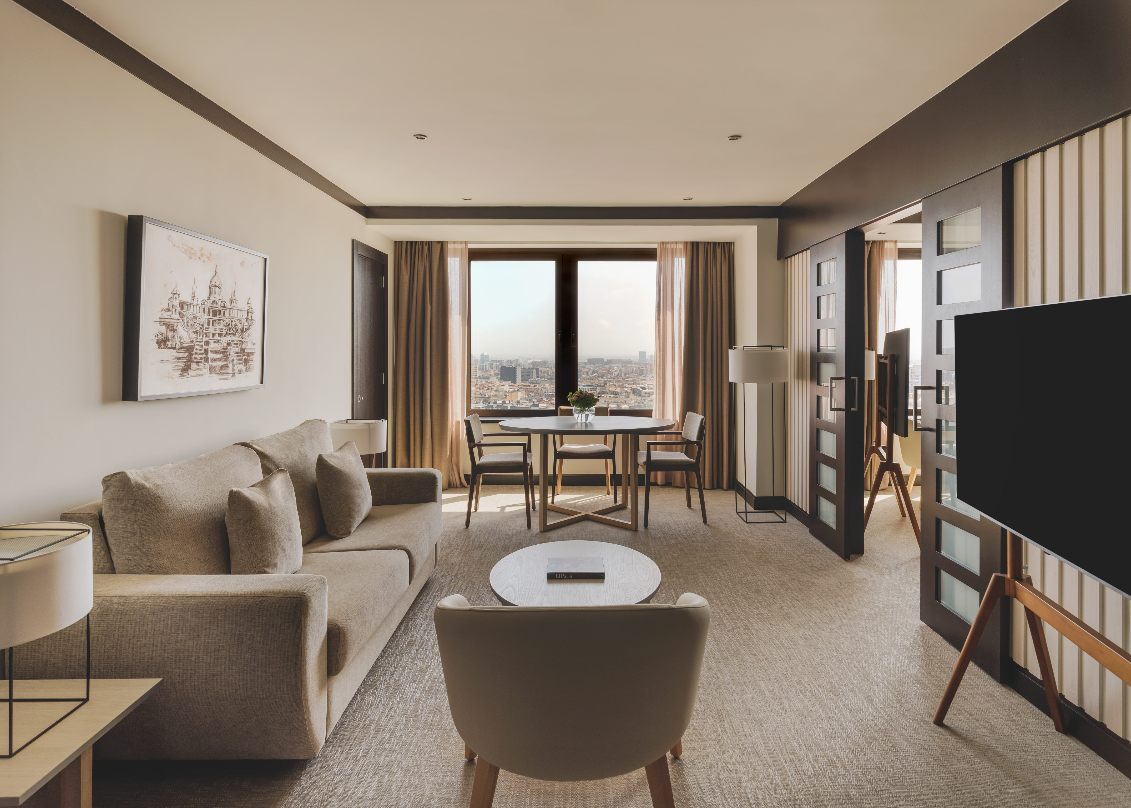 Suite de lujo con sala, sofá, mesa de comedor y vistas panorámicas a la ciudad.