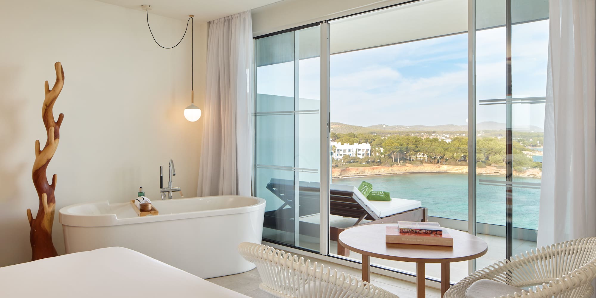 Modern hotel suite with sea view balcony, freestanding tub, and coastal scenery.