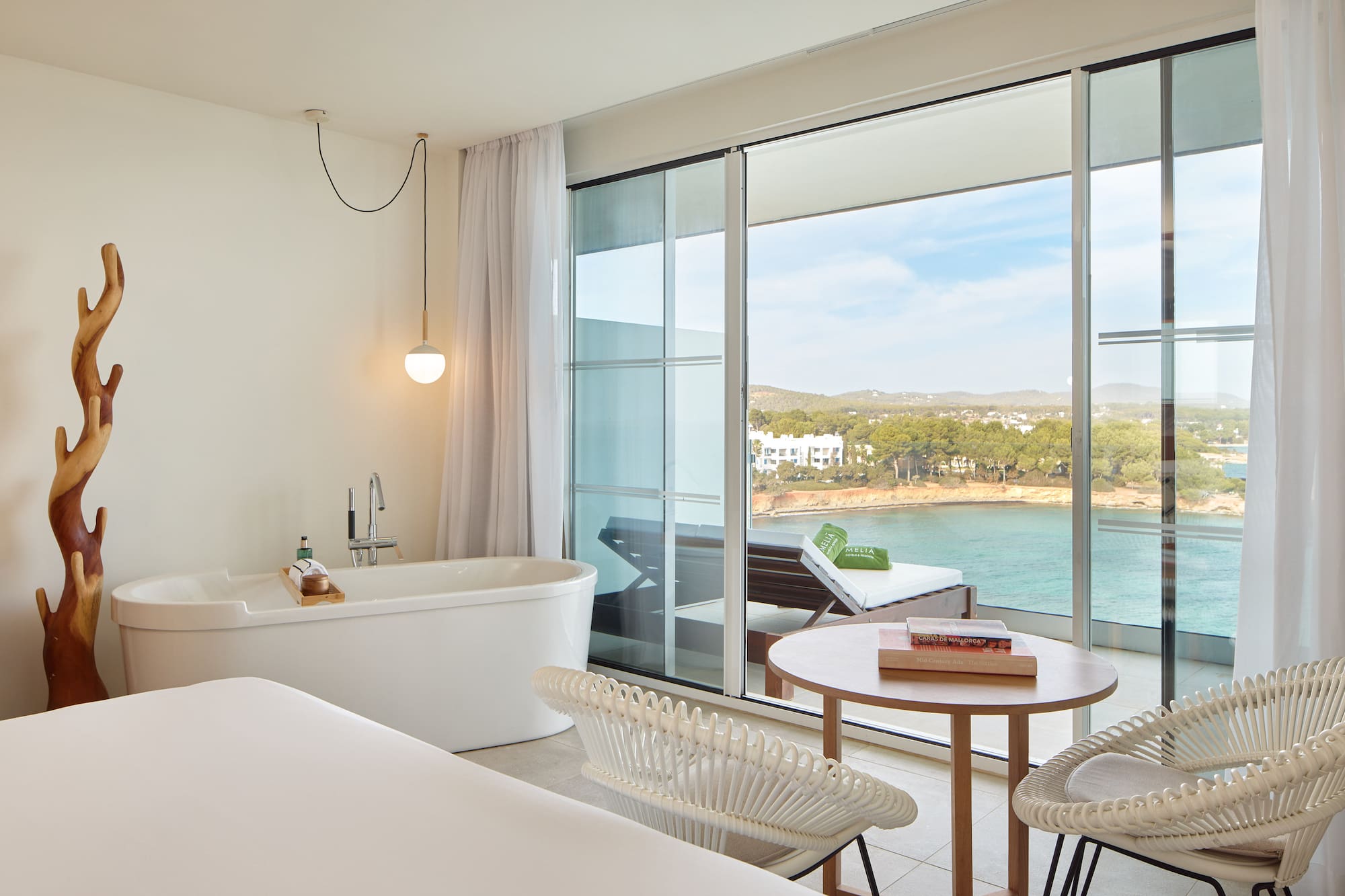 Modern hotel suite with sea view balcony, freestanding tub, and coastal scenery.