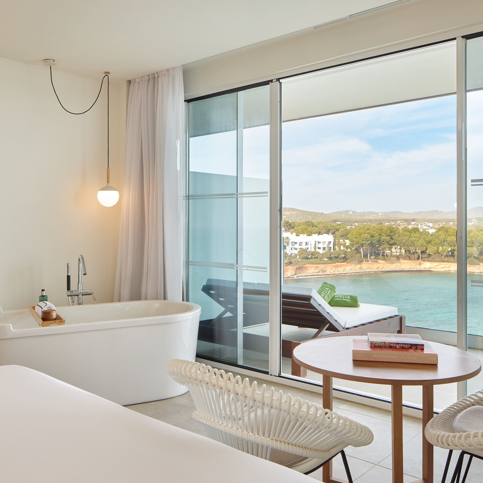 Modern hotel suite with sea view balcony, freestanding tub, and coastal scenery.