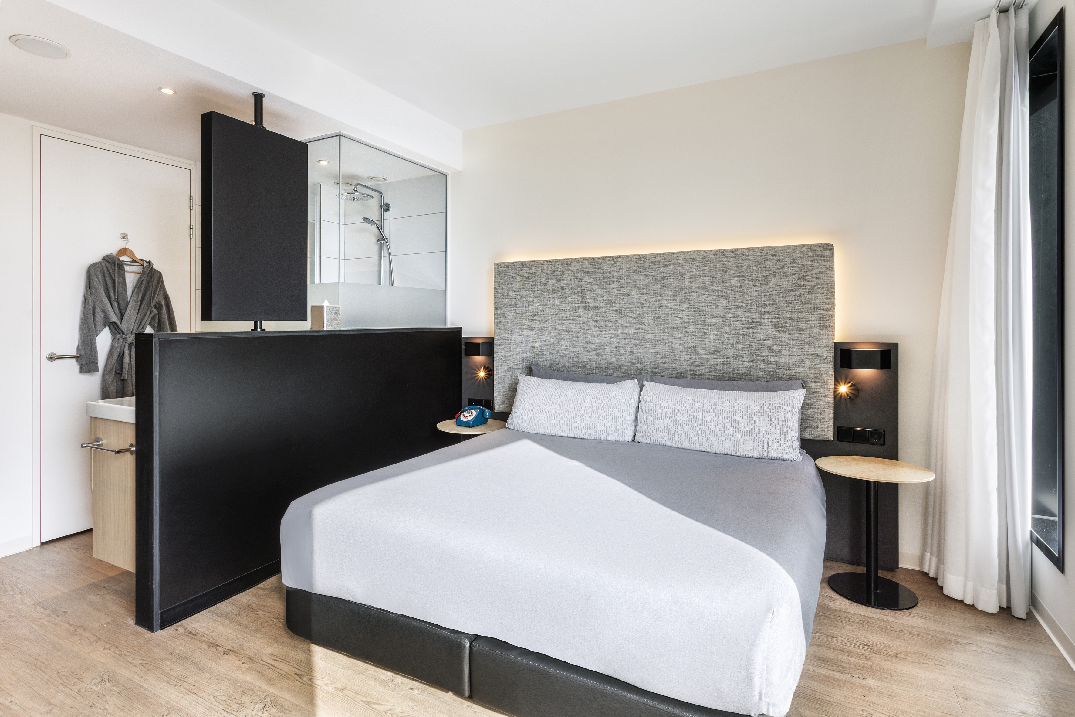 Modern hotel room with comfortable bed, backlit headboard, and integrated shower.