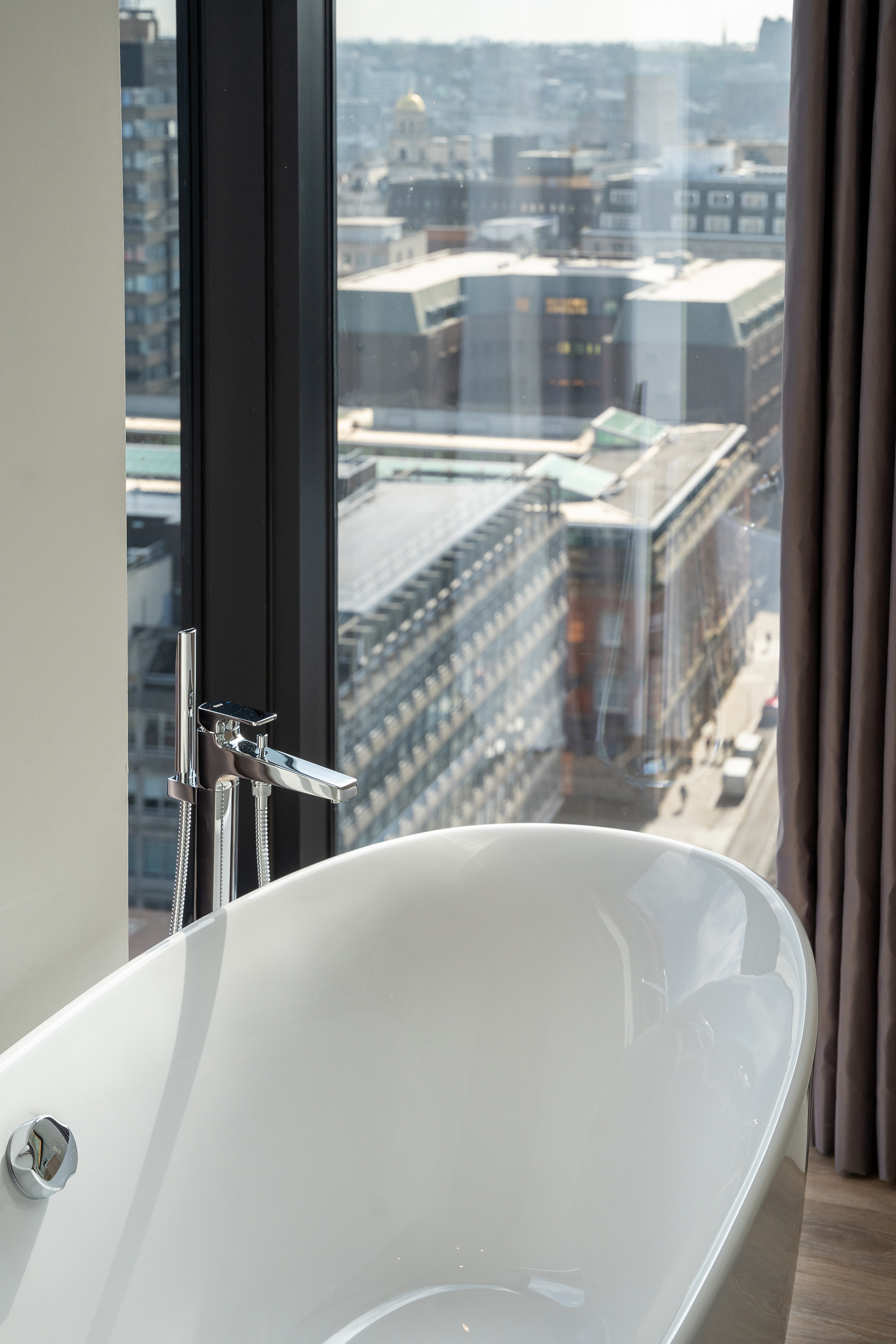 Modern white freestanding bathtub with city view from large window.