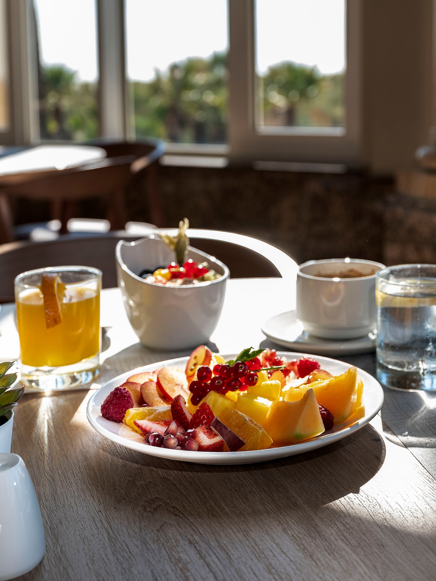 Healthy hotel breakfast with fresh fruit, juice, and coffee on a sunlit table.