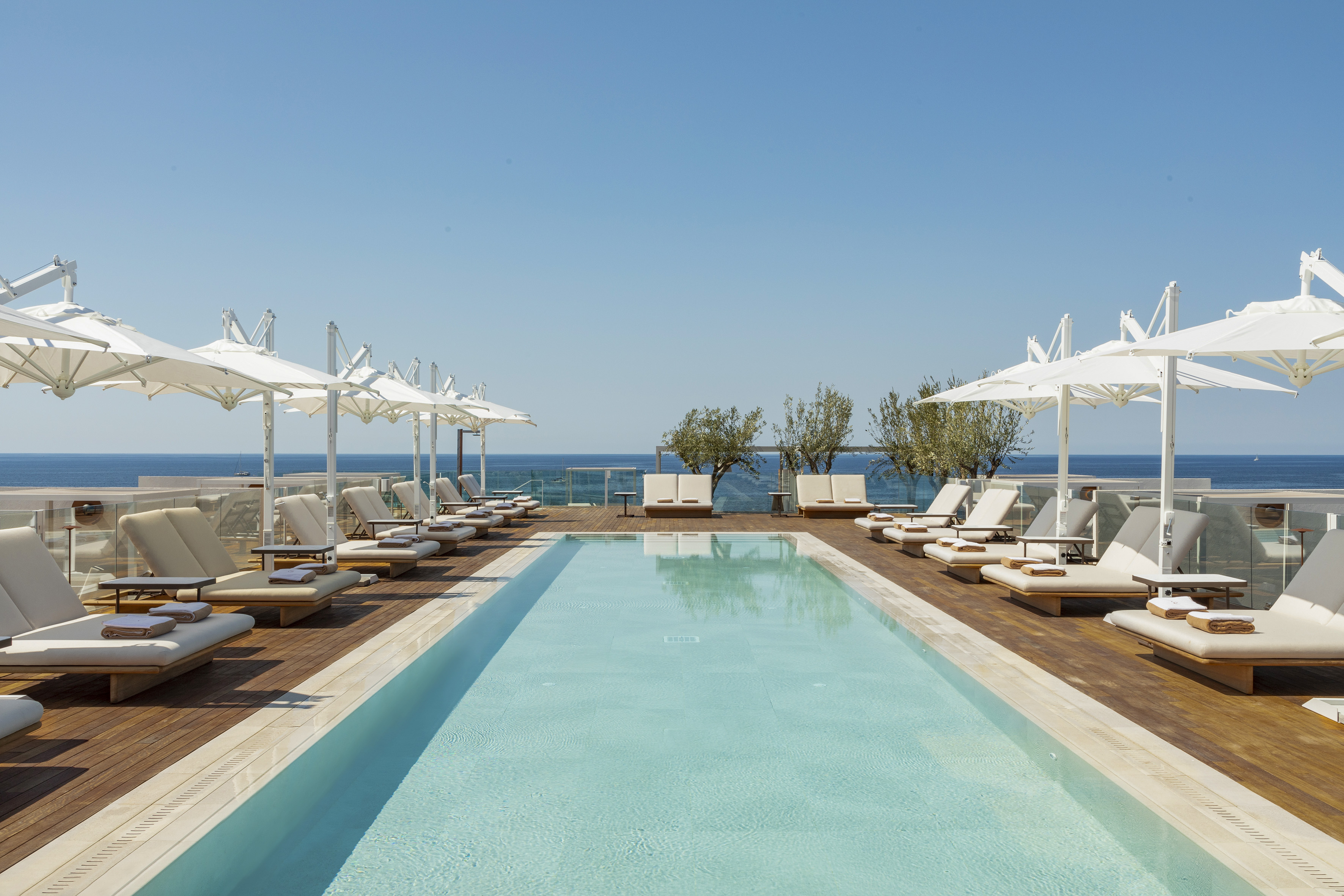 Luxury resort rooftop pool, ocean view, sun loungers, and white umbrellas.
