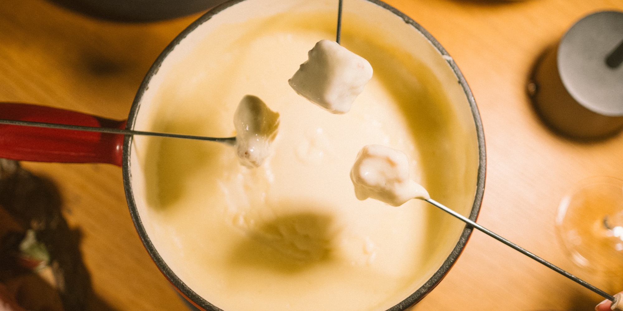 Hands dipping bread into cheese fondue, surrounded by appetizers on wooden table.