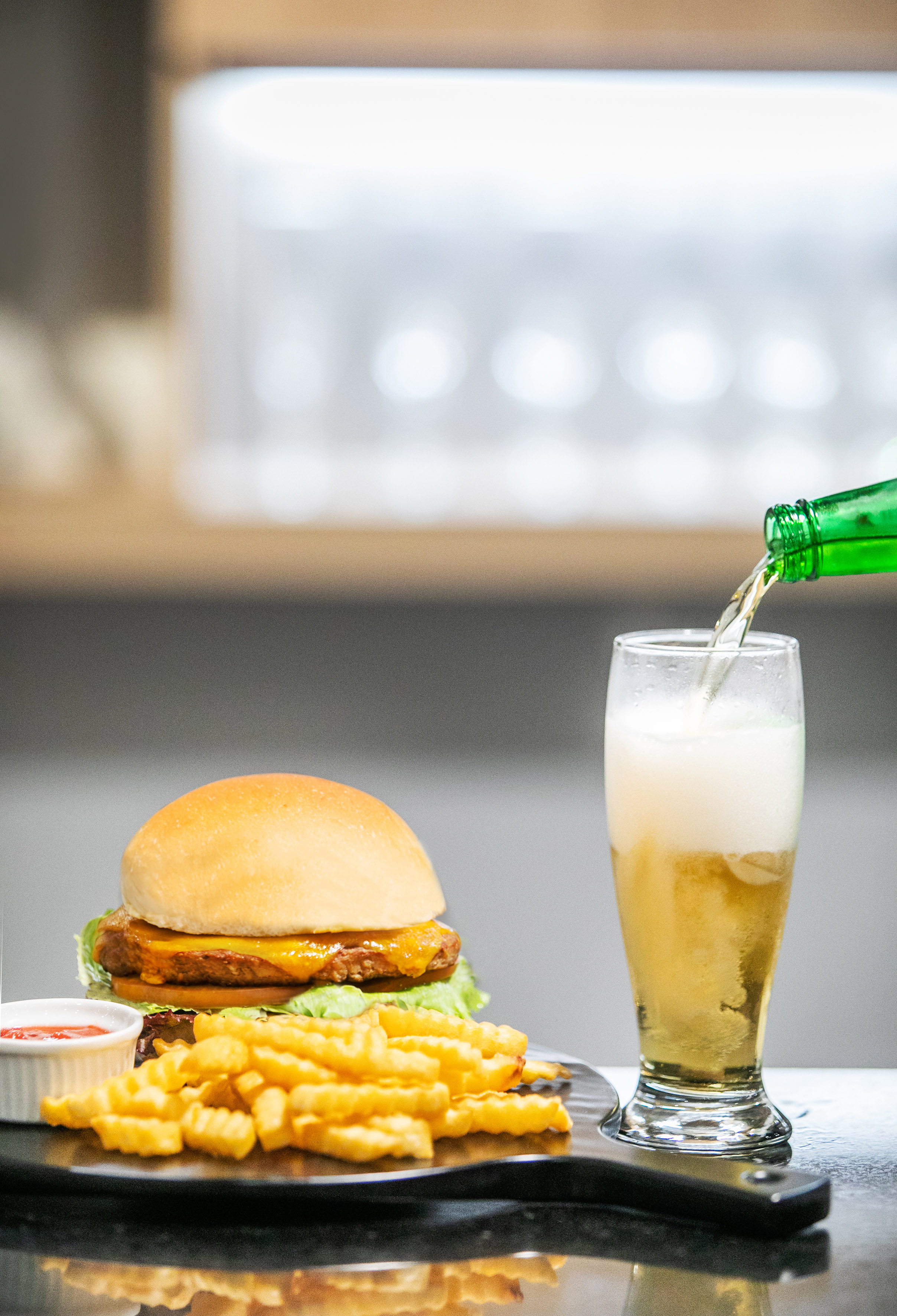 Cheeseburger with crinkle fries and ketchup, beer being poured into a glass.