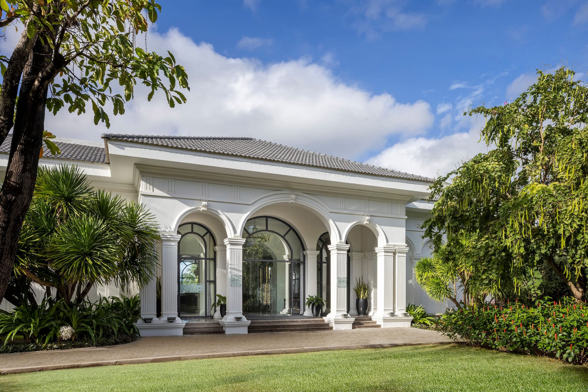 Luxury resort entrance with white arches, columns, green lawn, tropical garden.