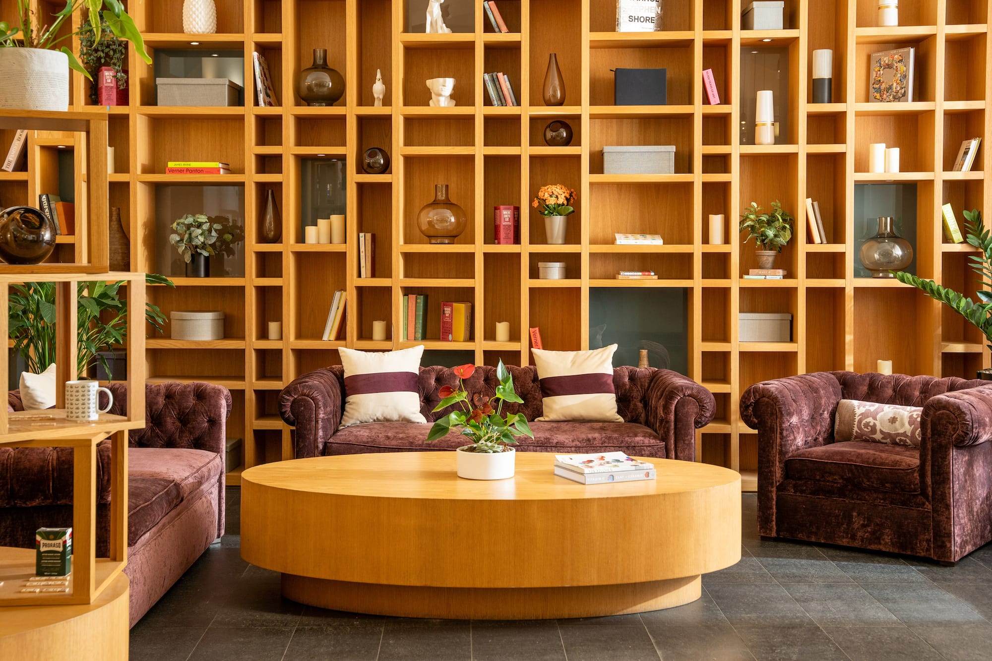 Lounge with large wooden shelving, velvet sofas, and round coffee table.