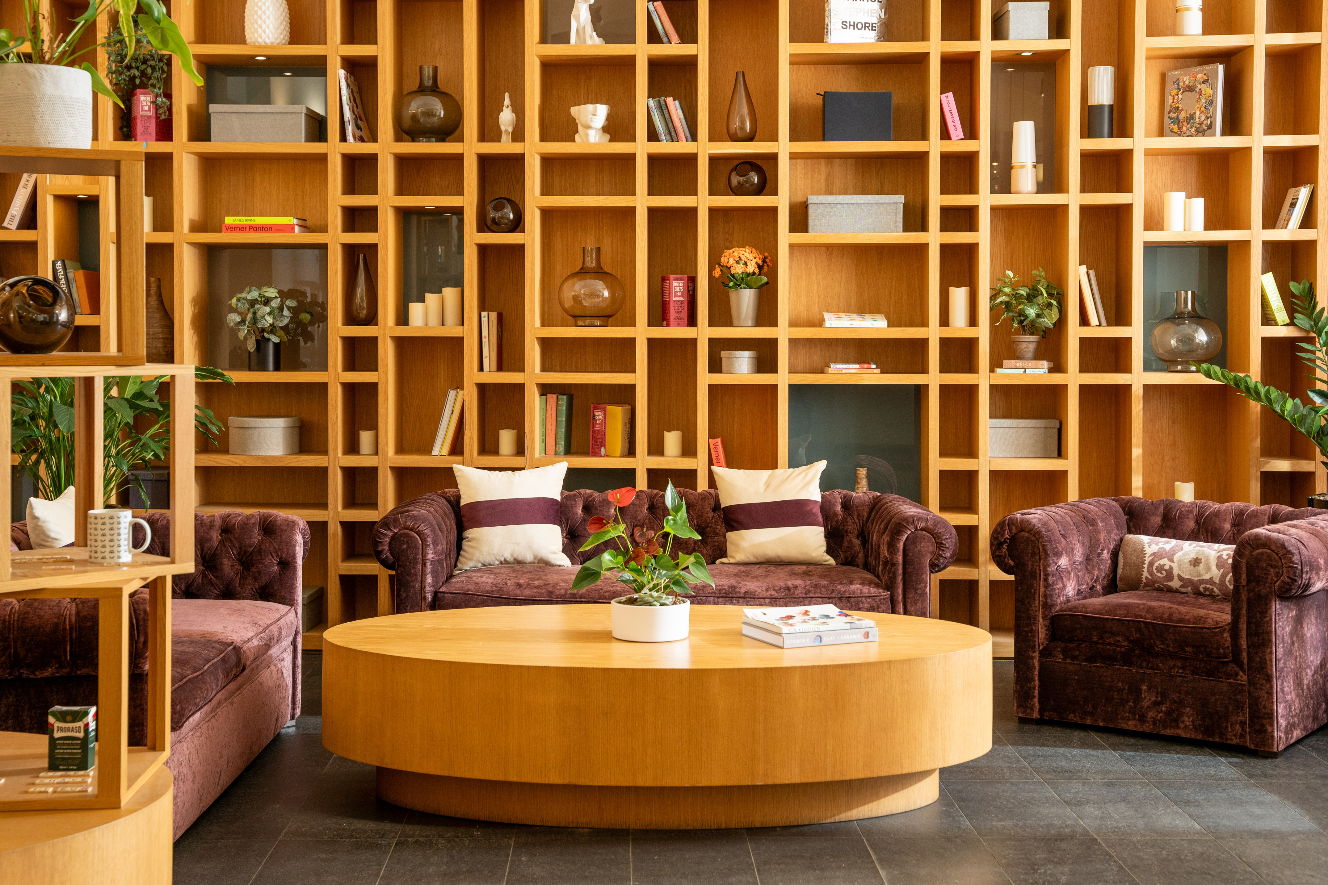 Lounge with large wooden shelving, velvet sofas, and round coffee table.