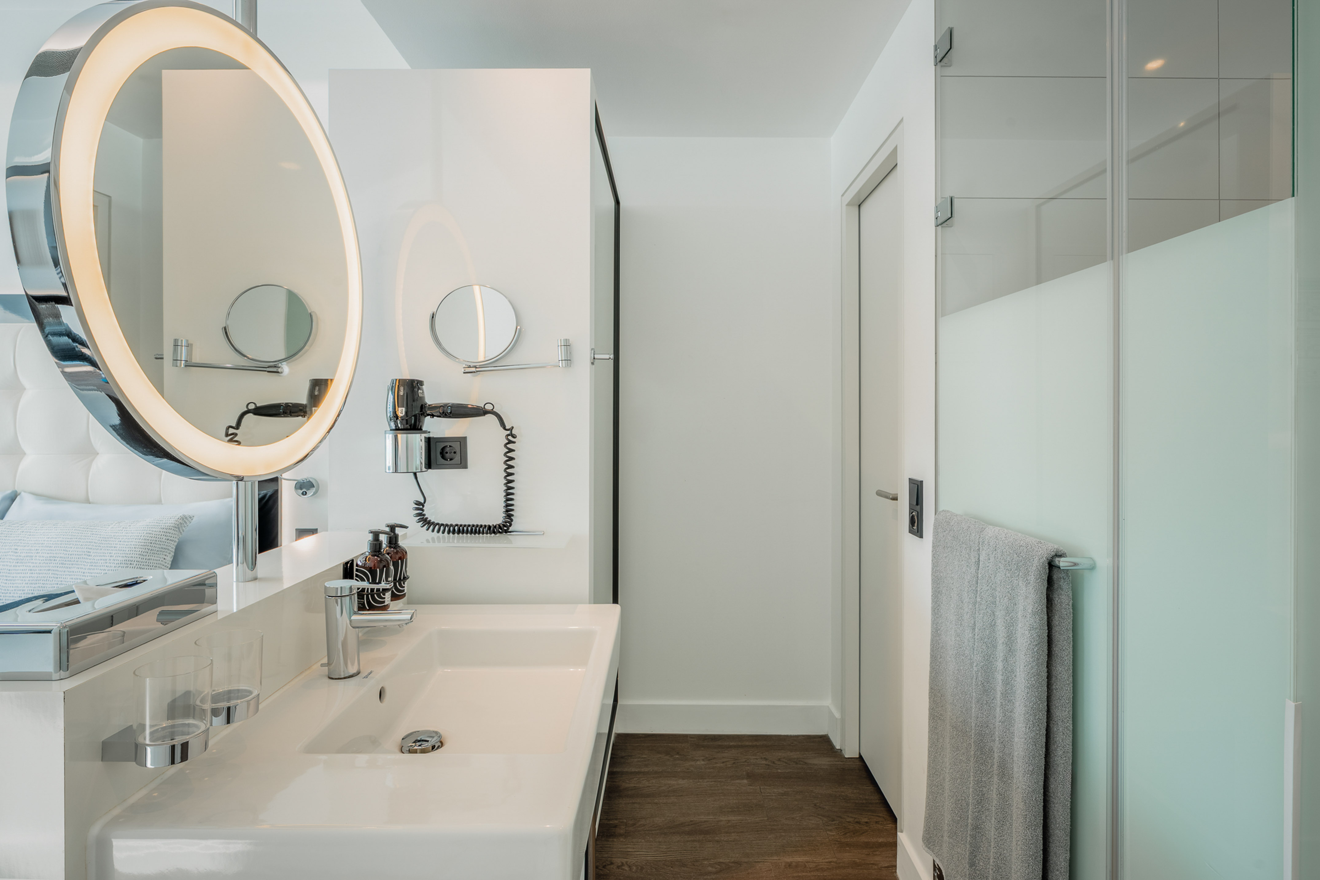 Modern hotel bathroom with illuminated vanity mirror, white sink, and shower.