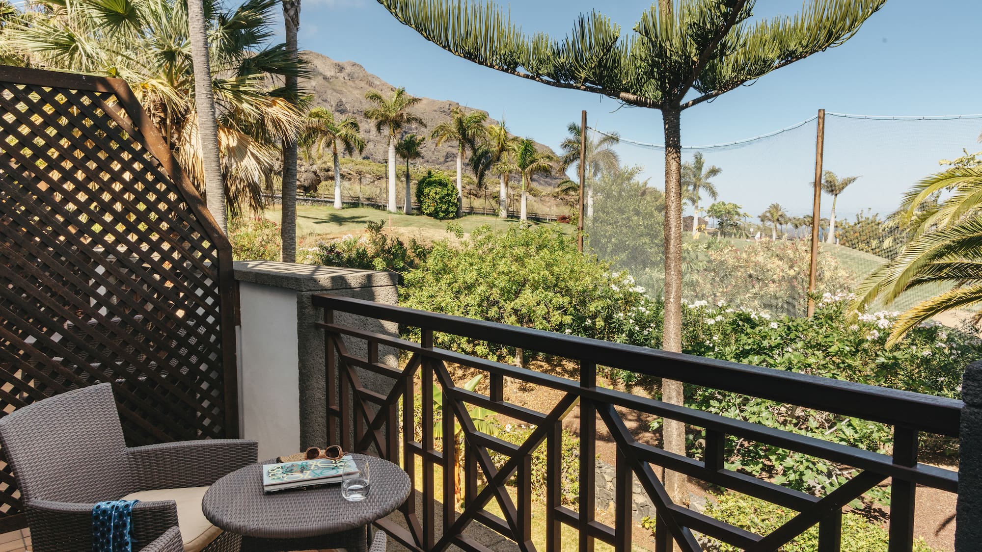 Balcony view of a tropical golf course with palm trees and mountains.