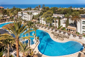 a swimming pool with palm trees and a building with a beach and blue sky