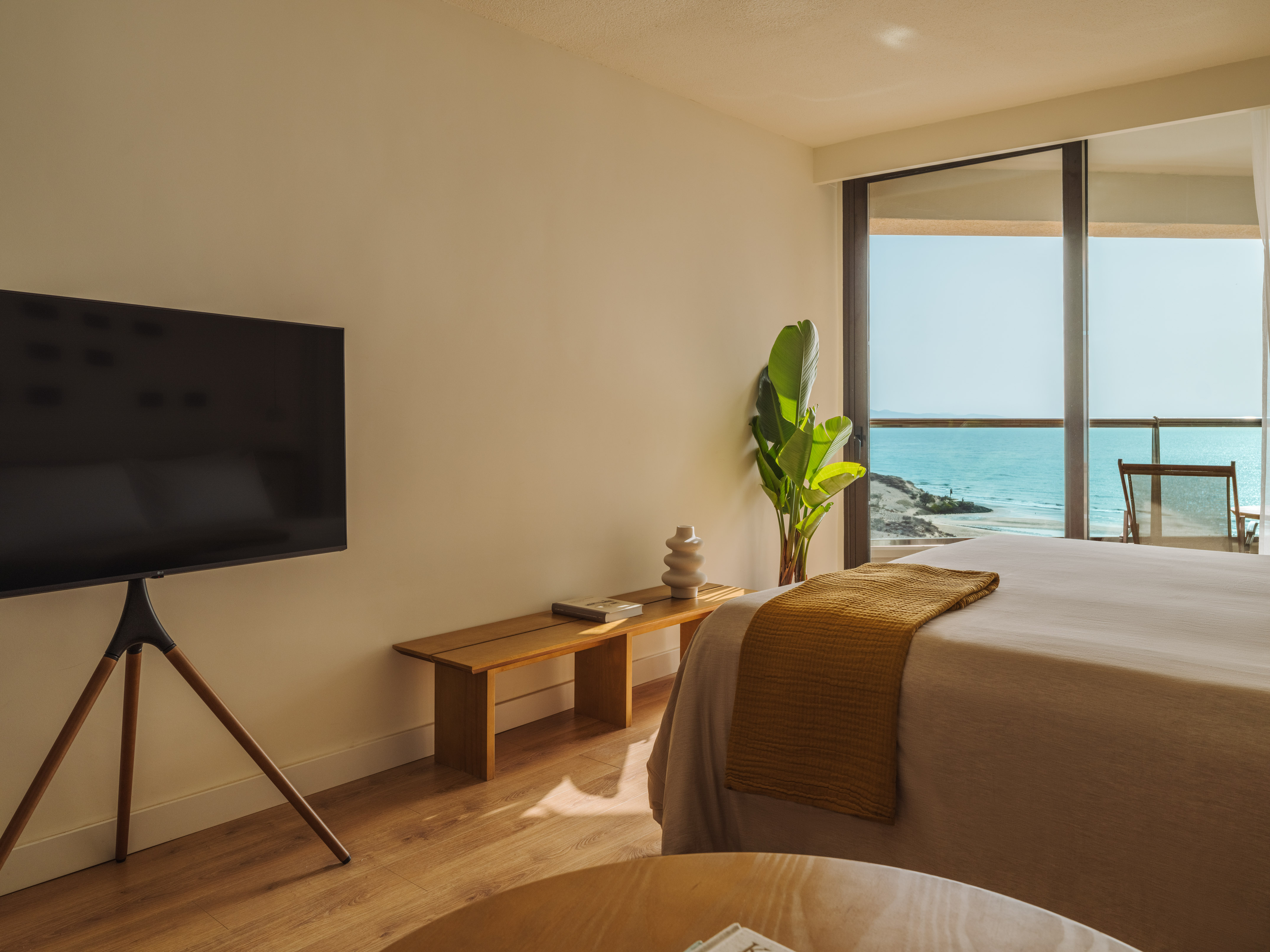 Hotel bedroom with sea view, large TV, and modern decor.