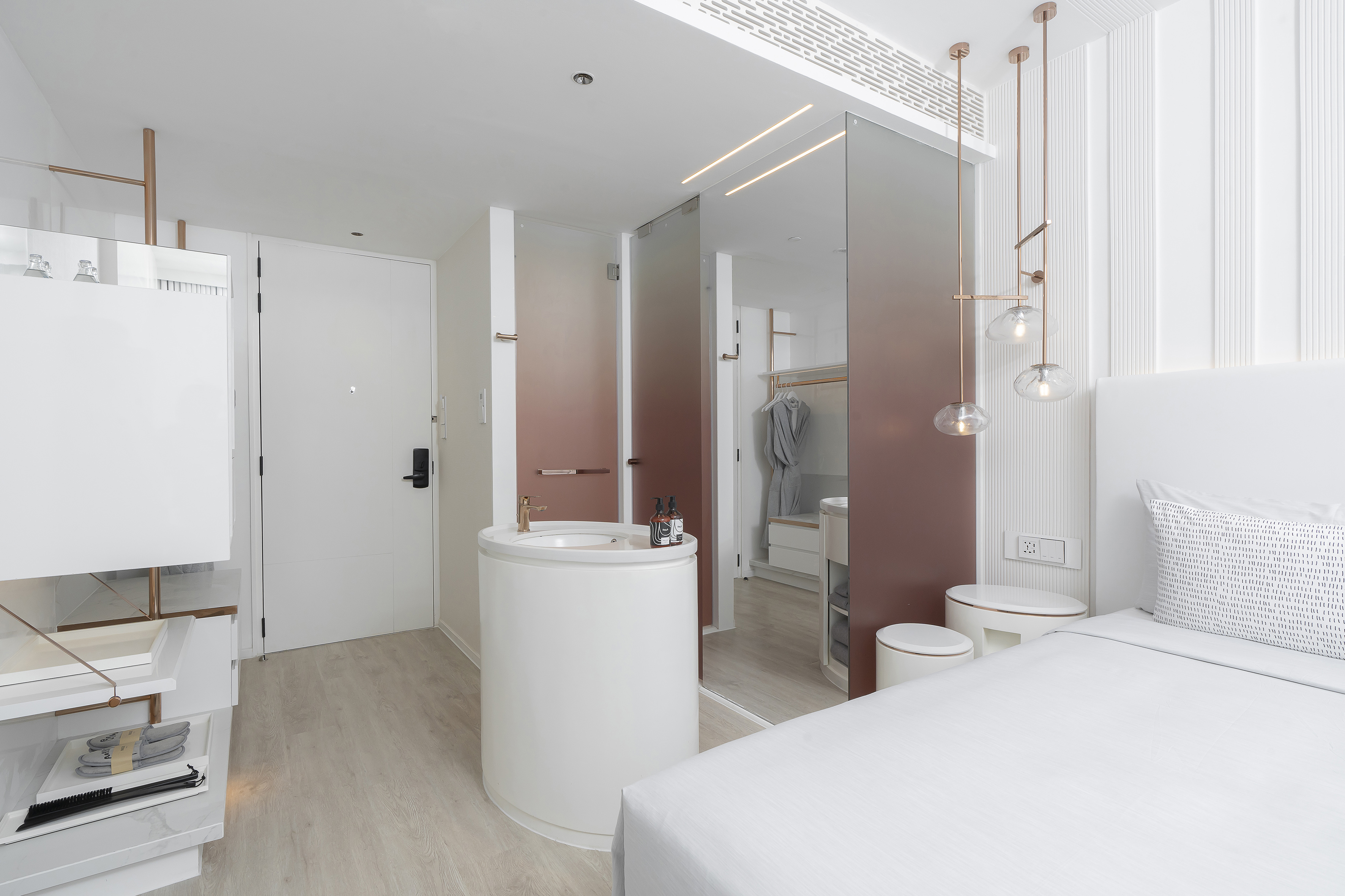 Modern hotel room with white bed, compact vanity, and rose gold fixtures.