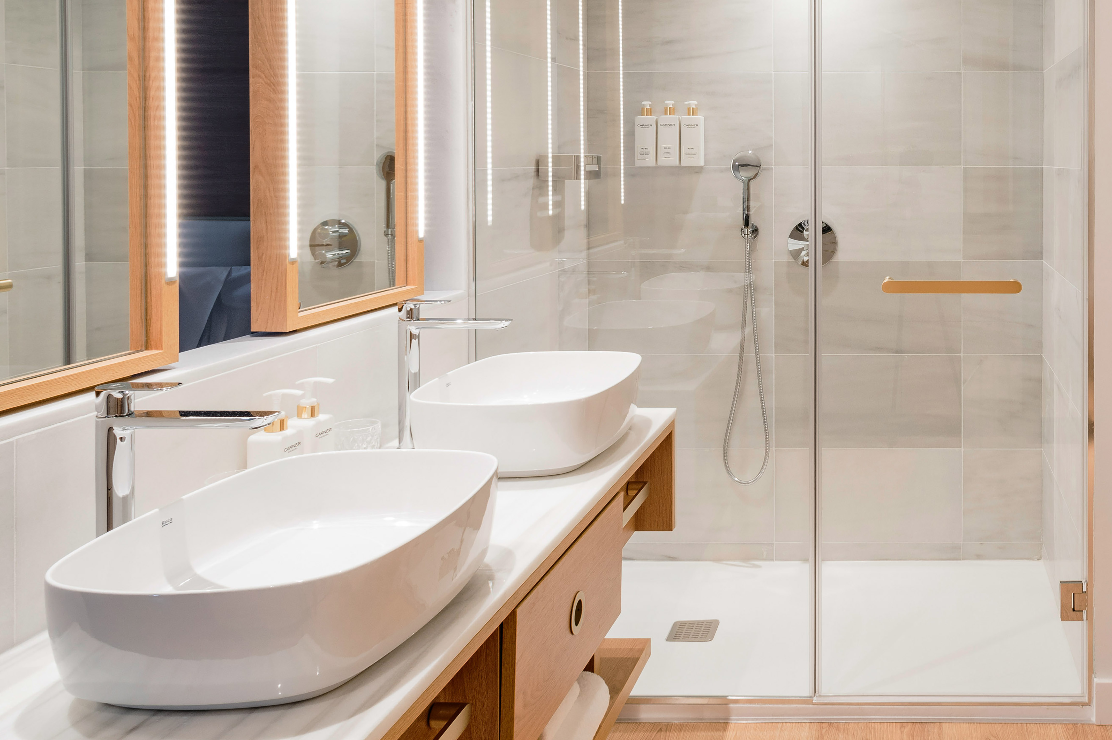 Modern bathroom with double vessel sinks, wood vanity, LED mirrors, and glass shower.