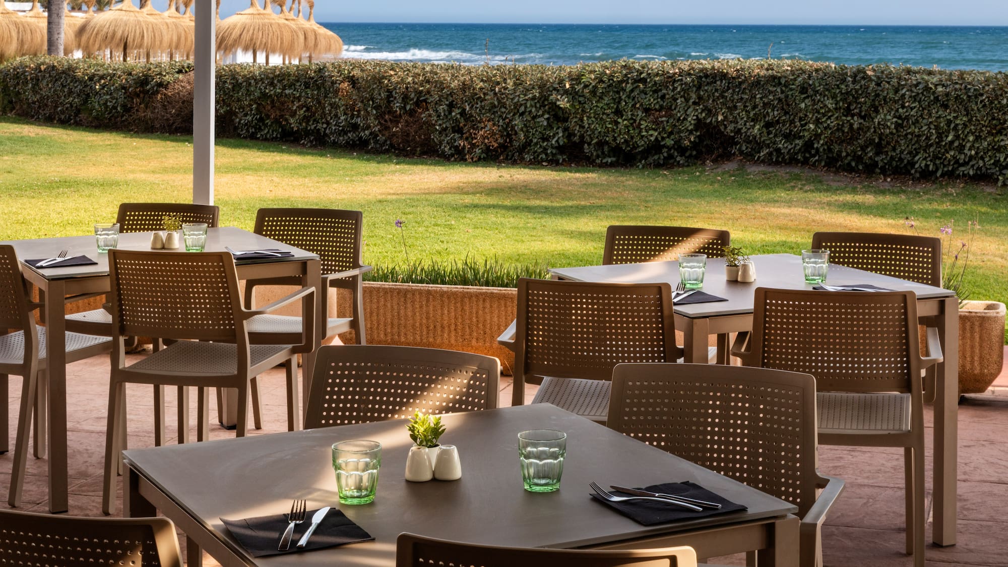a table and chairs outside with a beach in the background