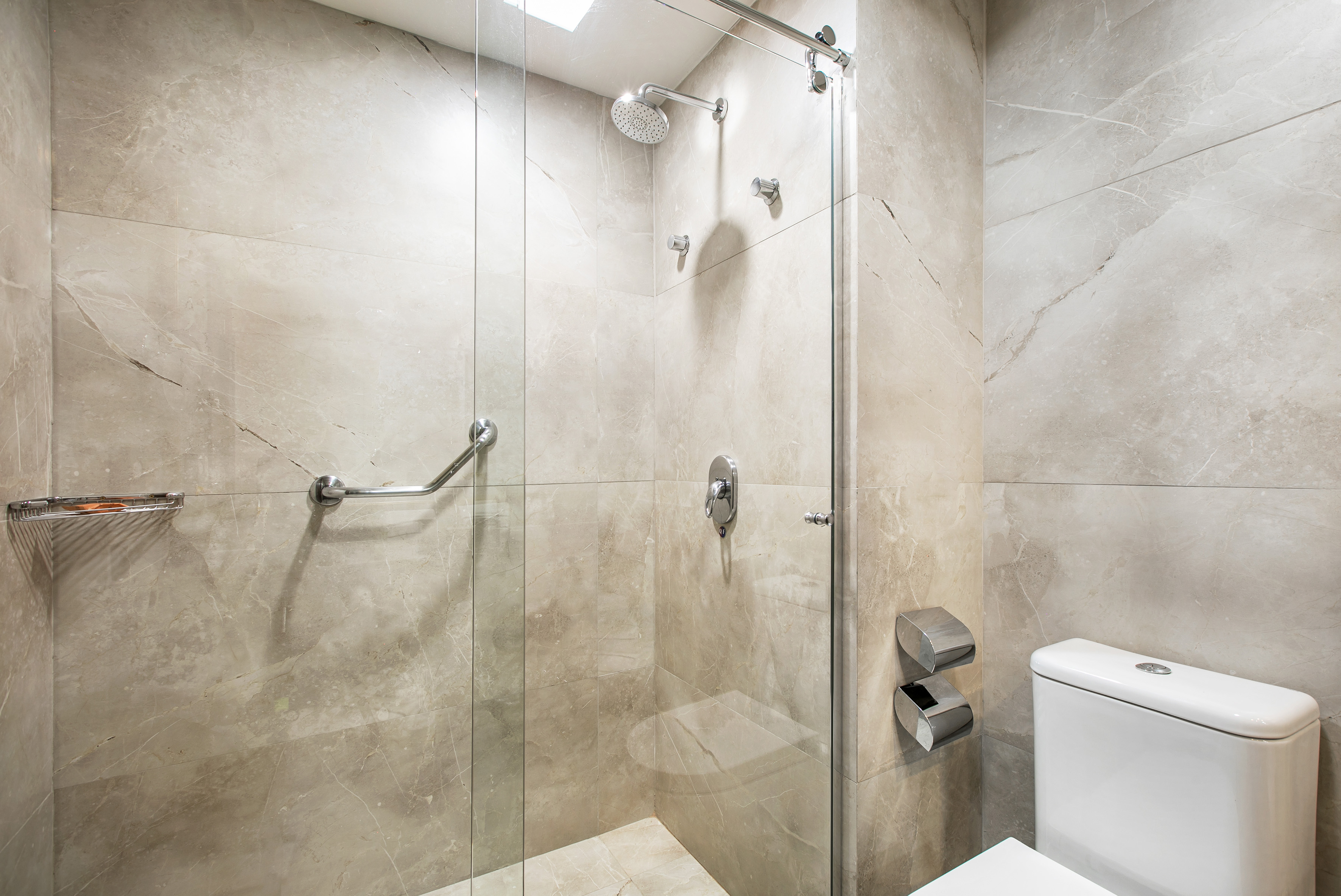 Modern hotel bathroom with accessible glass shower, grab bars, and toilet.