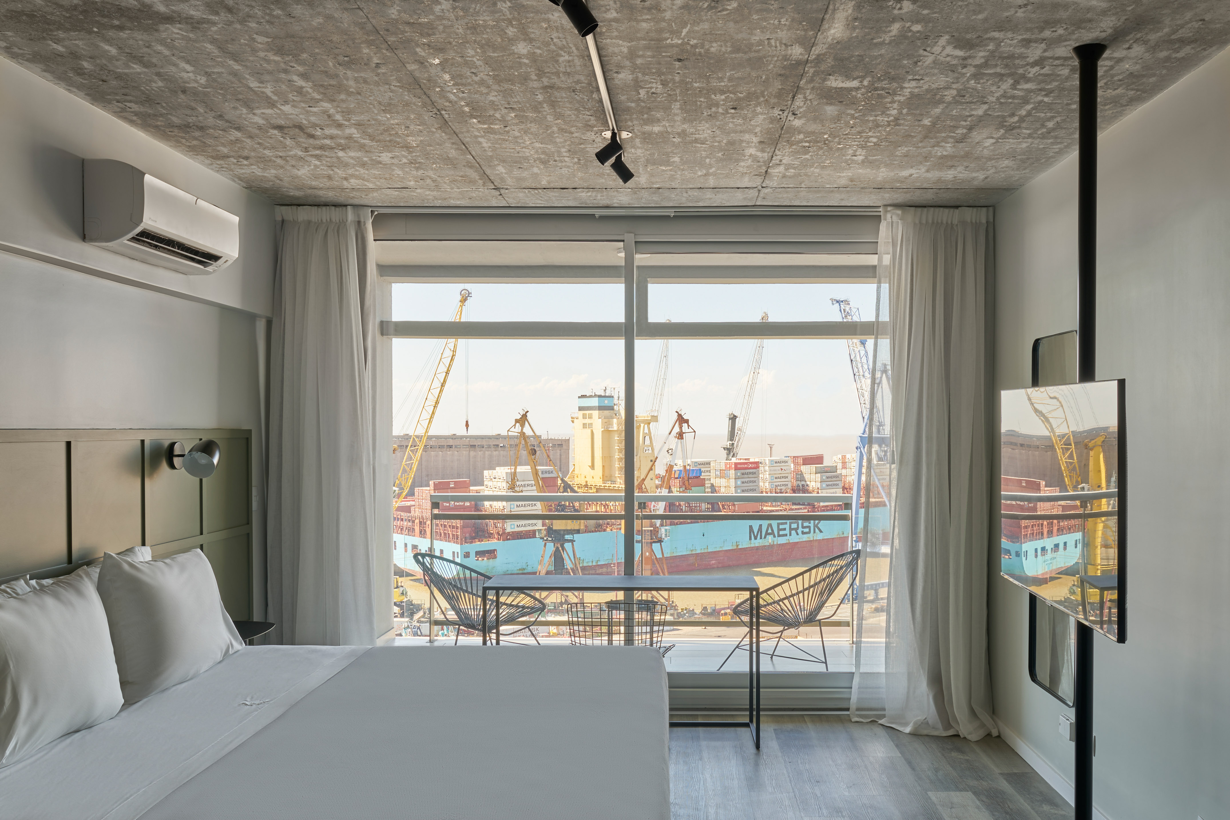 Modern hotel room with harbor view of a Maersk container ship and cranes.