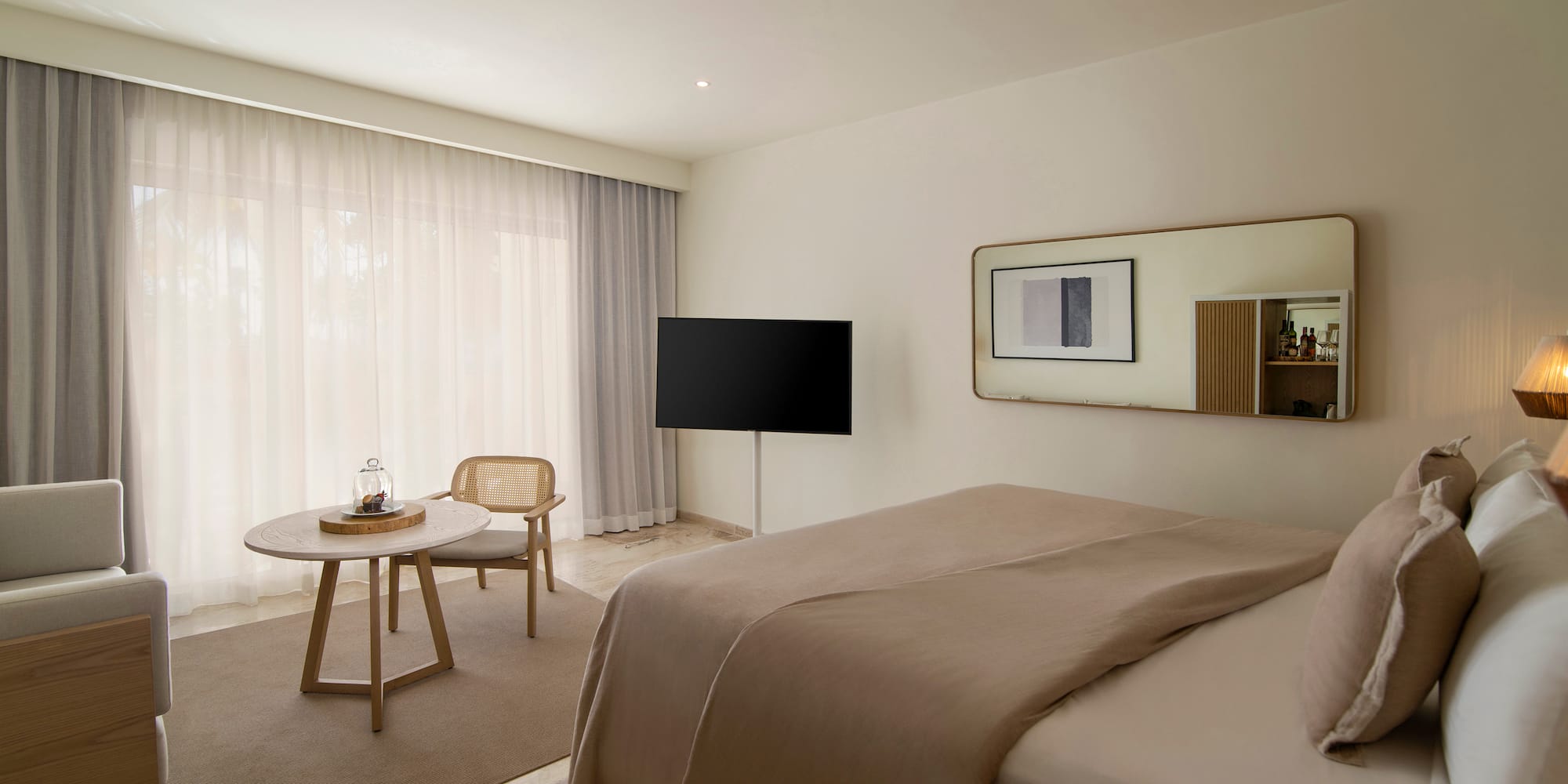 Modern hotel room with beige bed, TV, rattan chair, and large window.