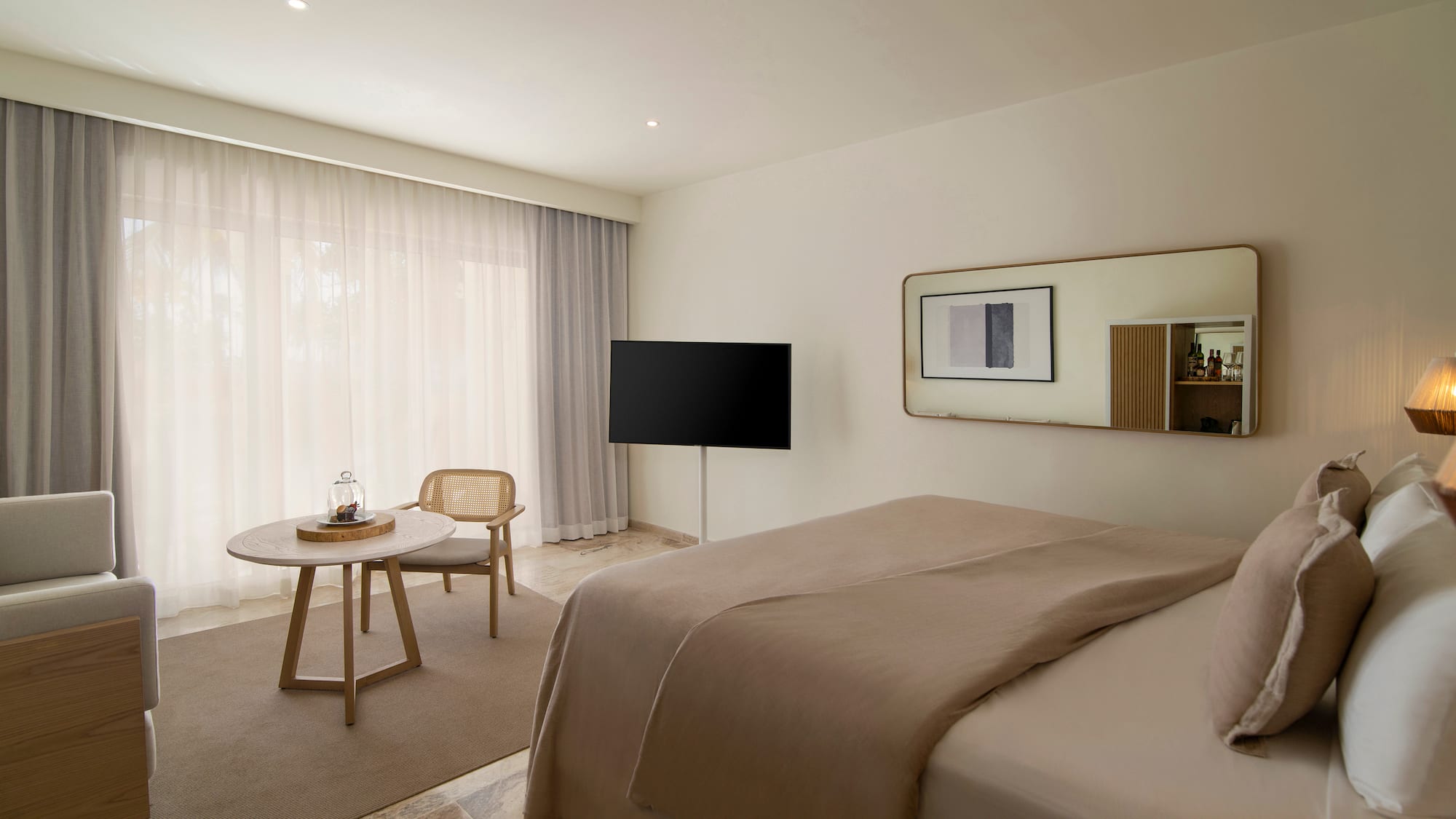 Modern hotel room with beige bed, TV, rattan chair, and large window.