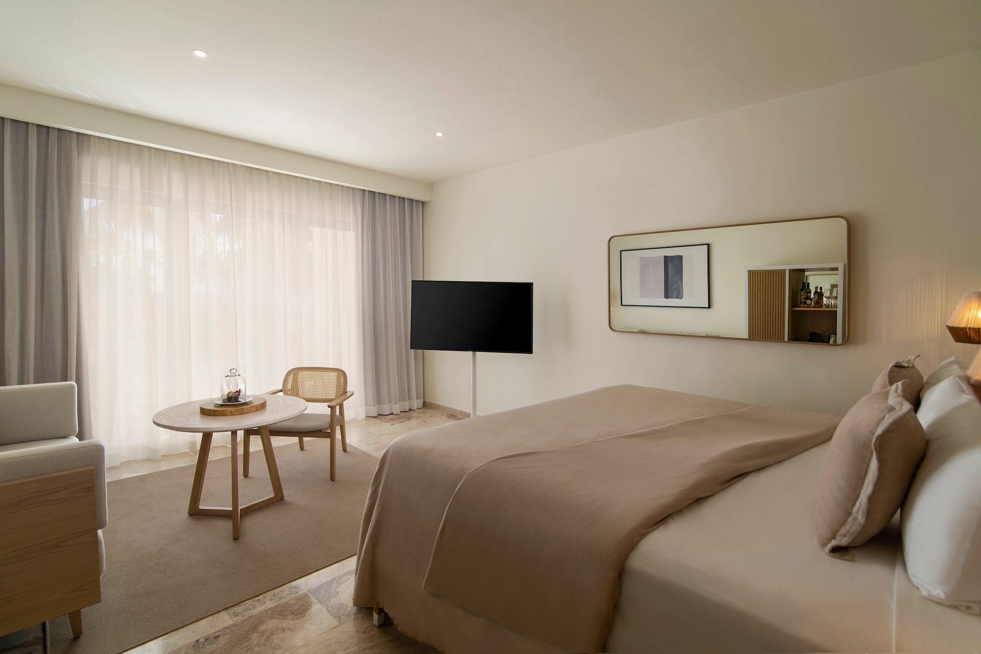 Modern hotel room with beige bed, TV, rattan chair, and large window.