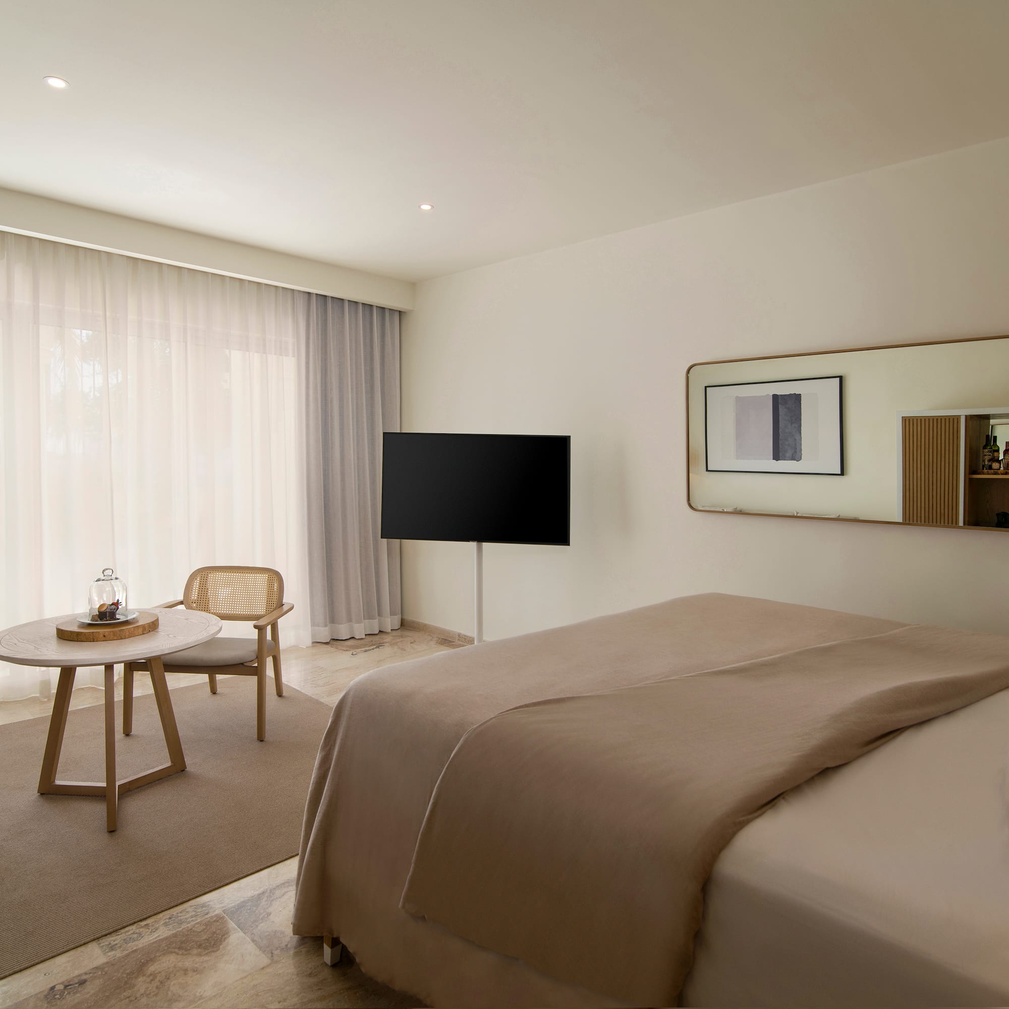 Modern hotel room with beige bed, TV, rattan chair, and large window.