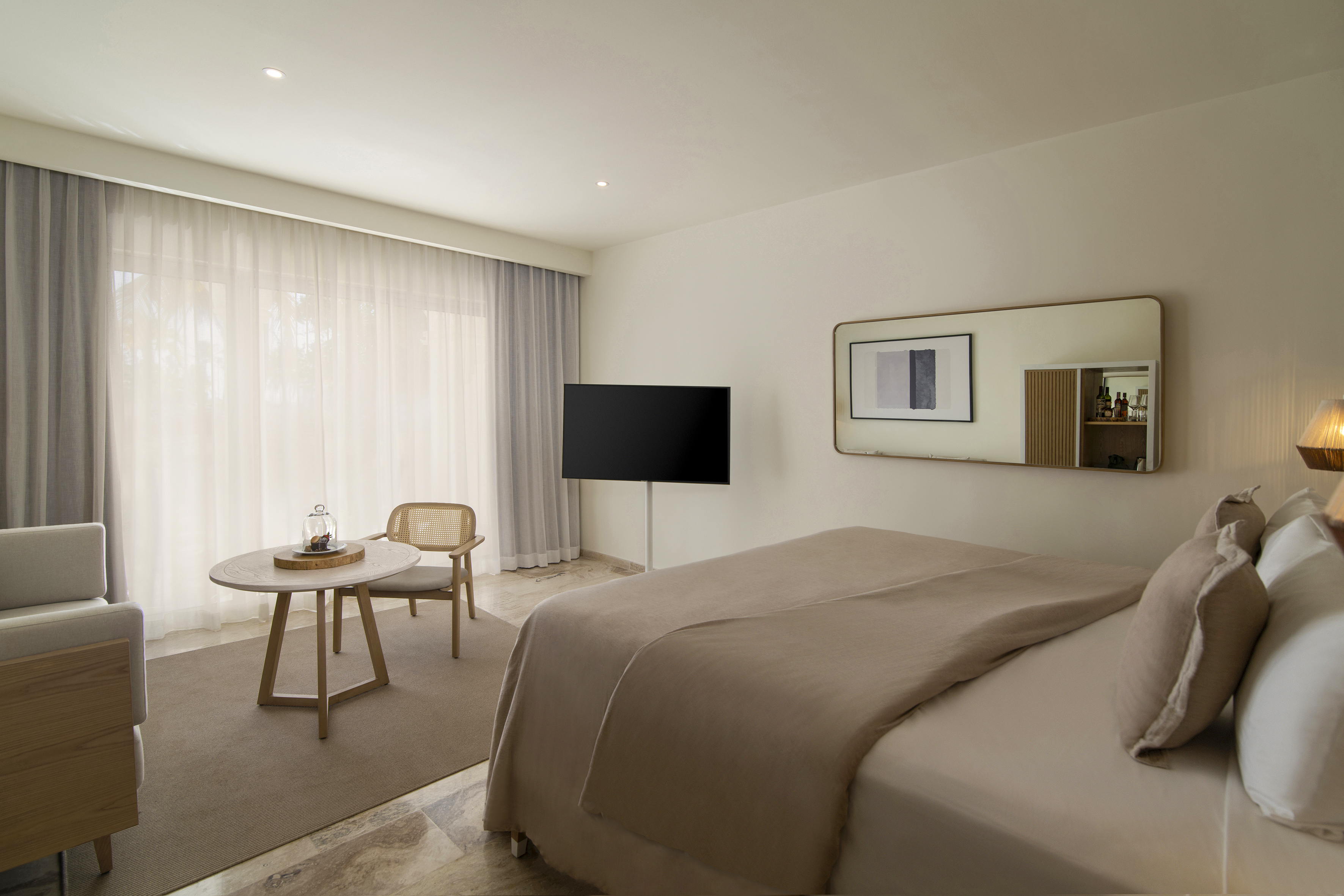 Modern hotel room with beige bed, TV, rattan chair, and large window.