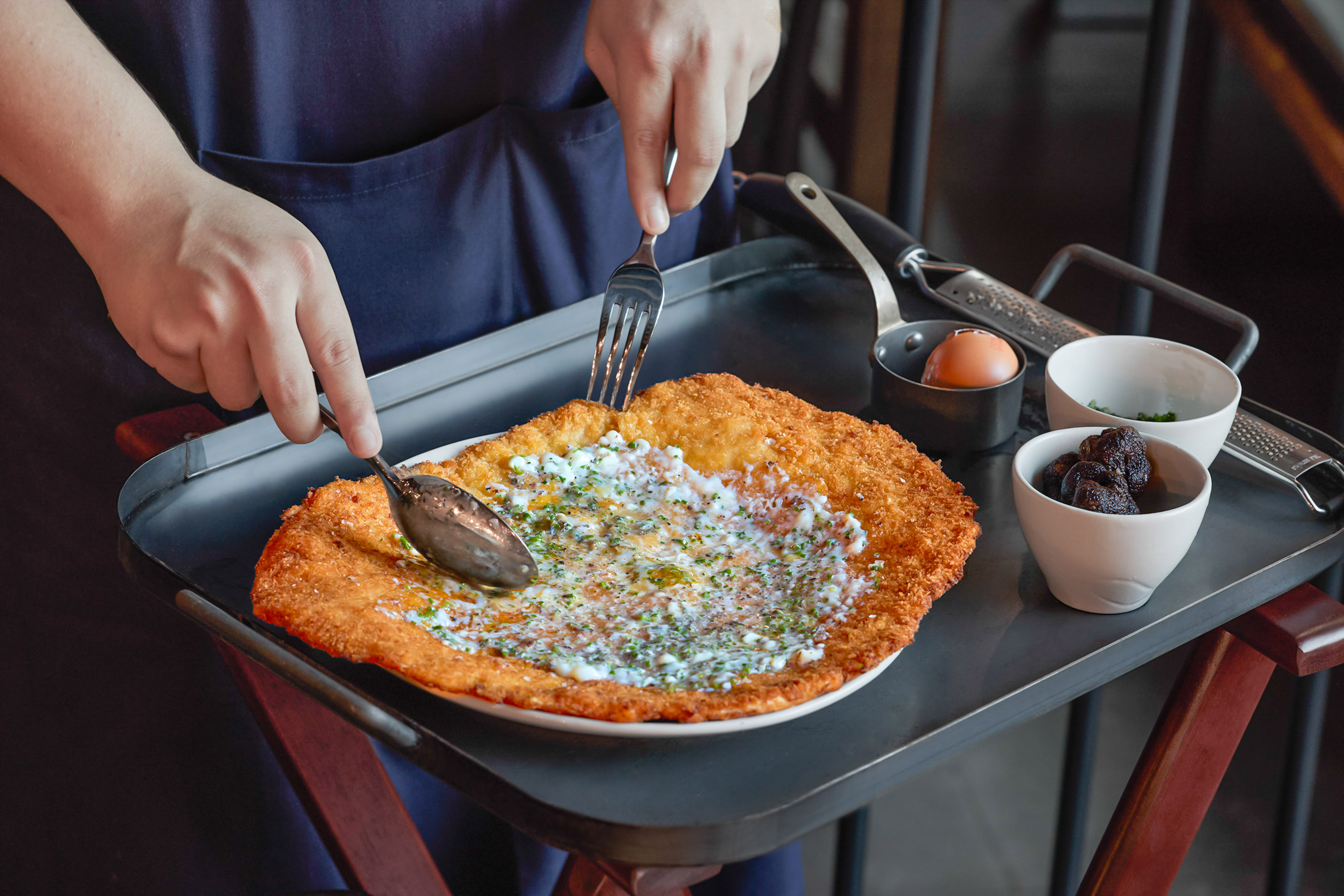 Chef serving crispy schnitzel with creamy sauce, truffles, and egg.