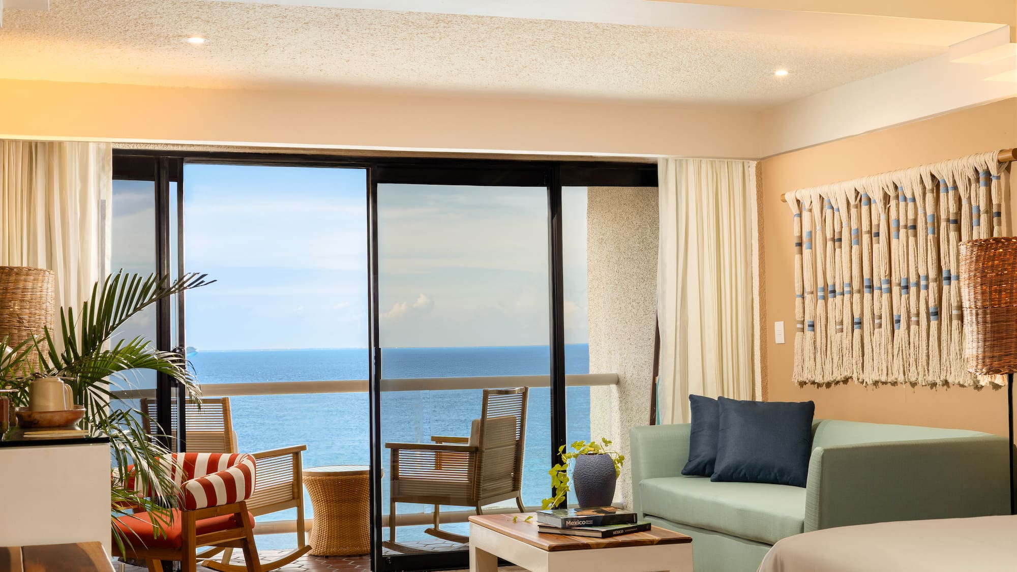 Ocean view hotel suite with balcony, living room, and tropical plants.