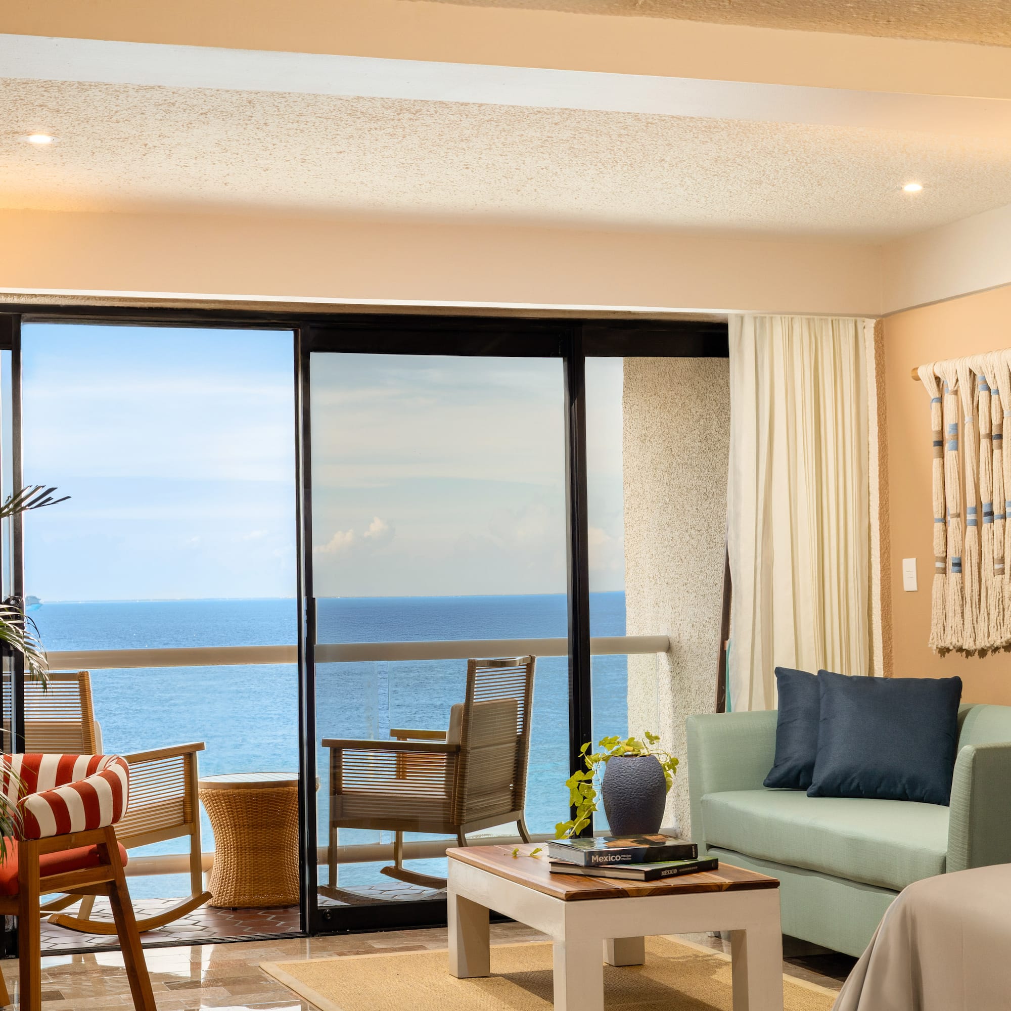Ocean view hotel suite with balcony, living room, and tropical plants.