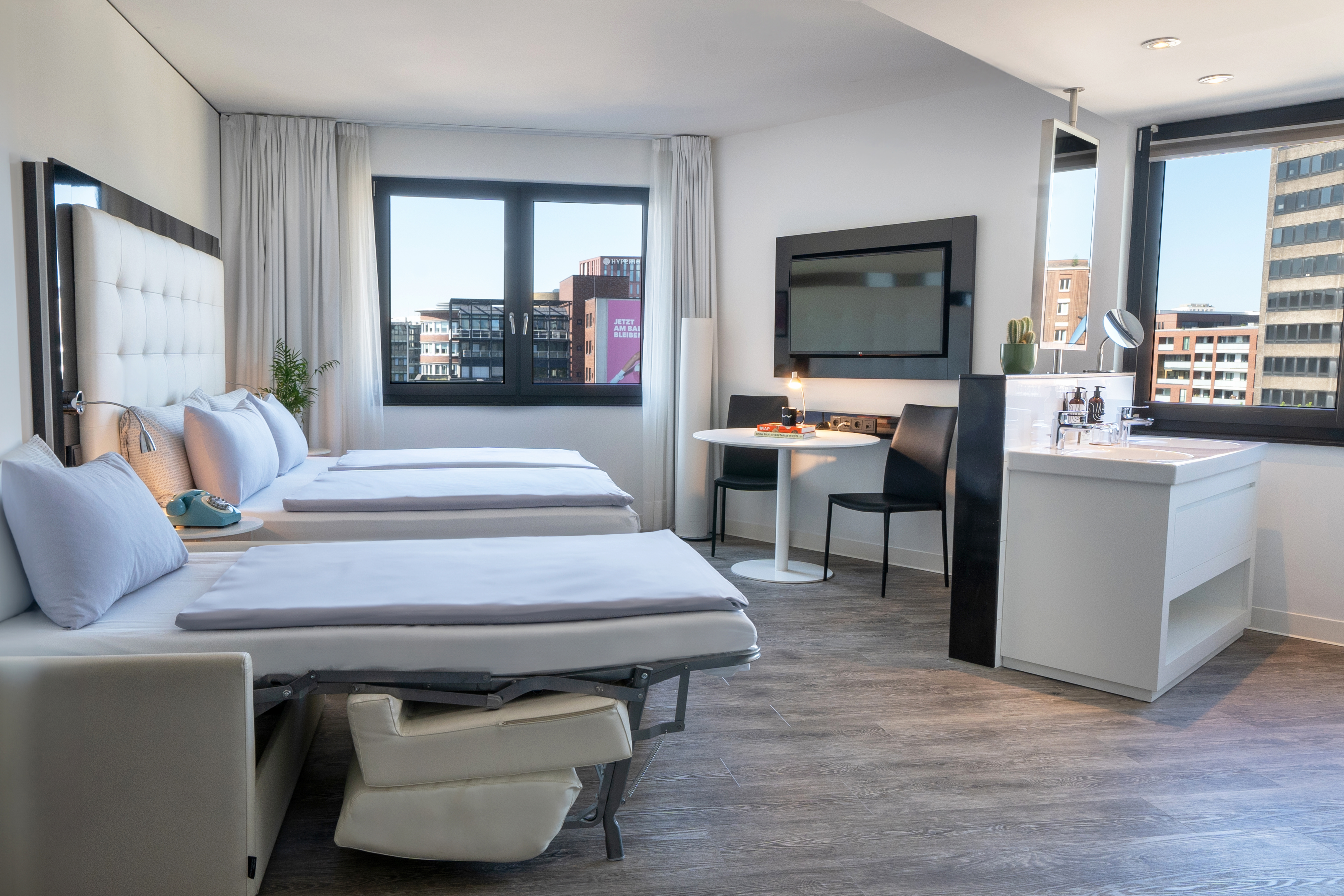Stylish hotel studio with two pull-out beds, city view window, TV, and vanity.