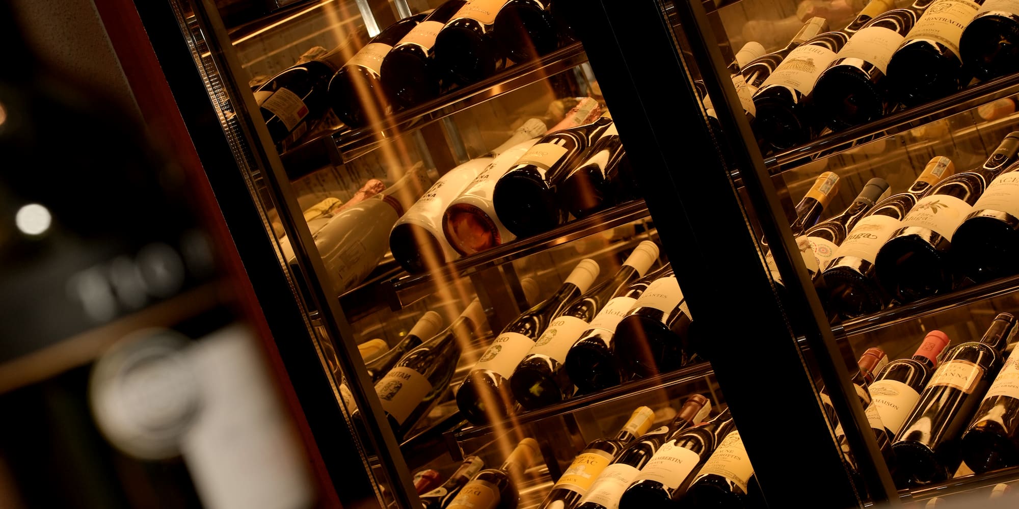 Vinoteca de lujo con hileras de botellas de vino y termostato 9.0°C, vela.