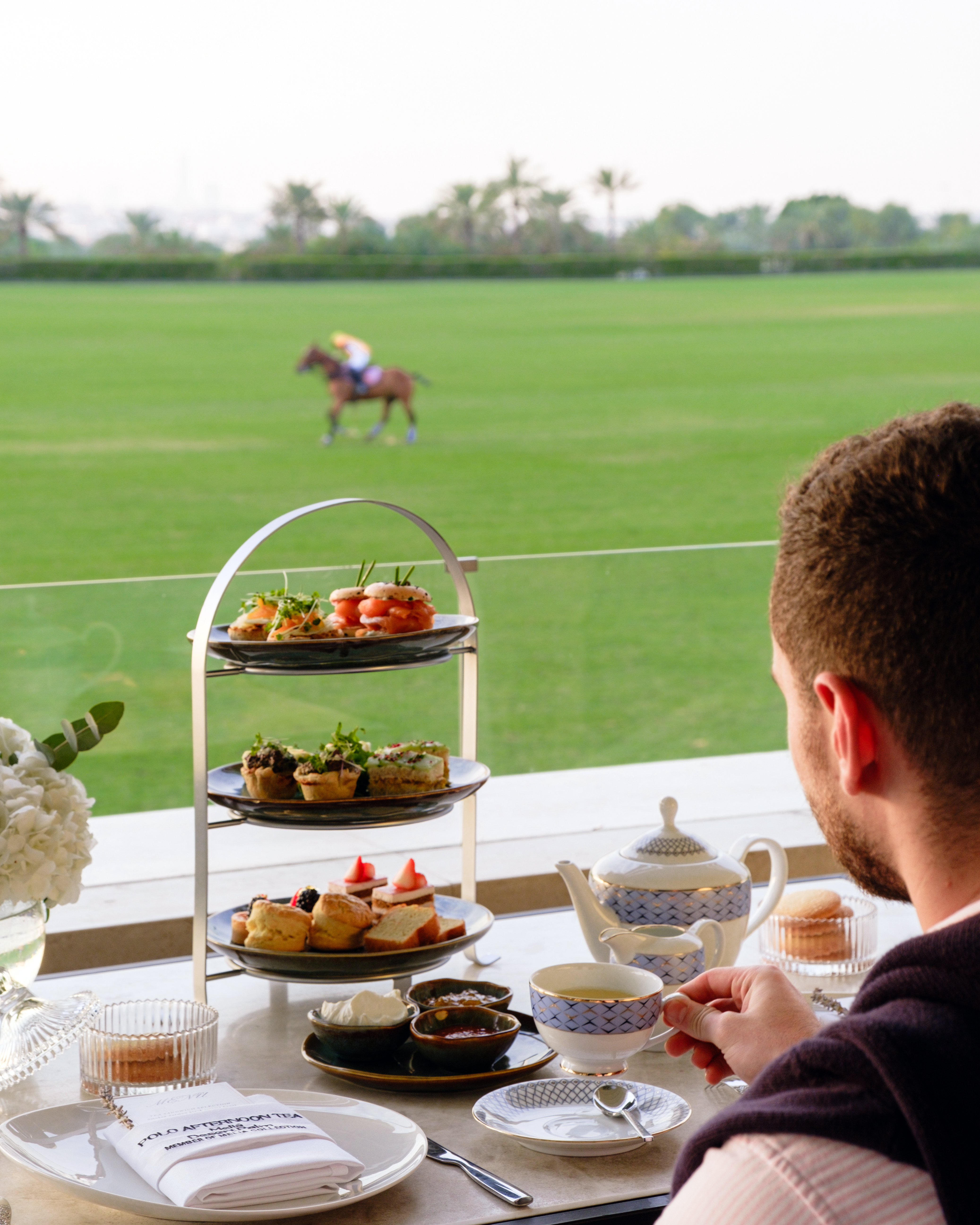 Man enjoying Polo Afternoon Tea with tiered stand overlooking a polo field.