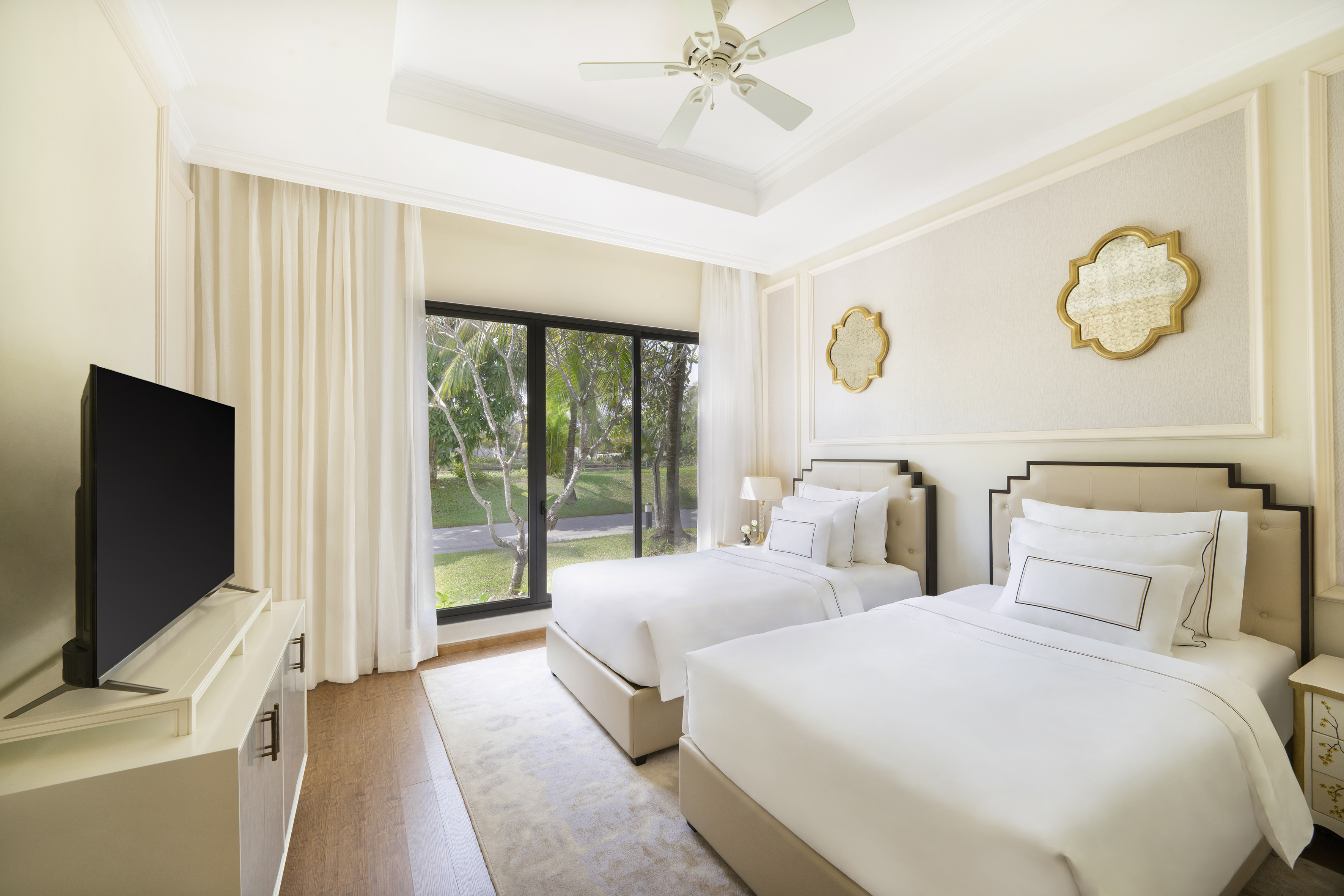 Bright hotel room with two twin beds, garden view, TV, and ceiling fan.