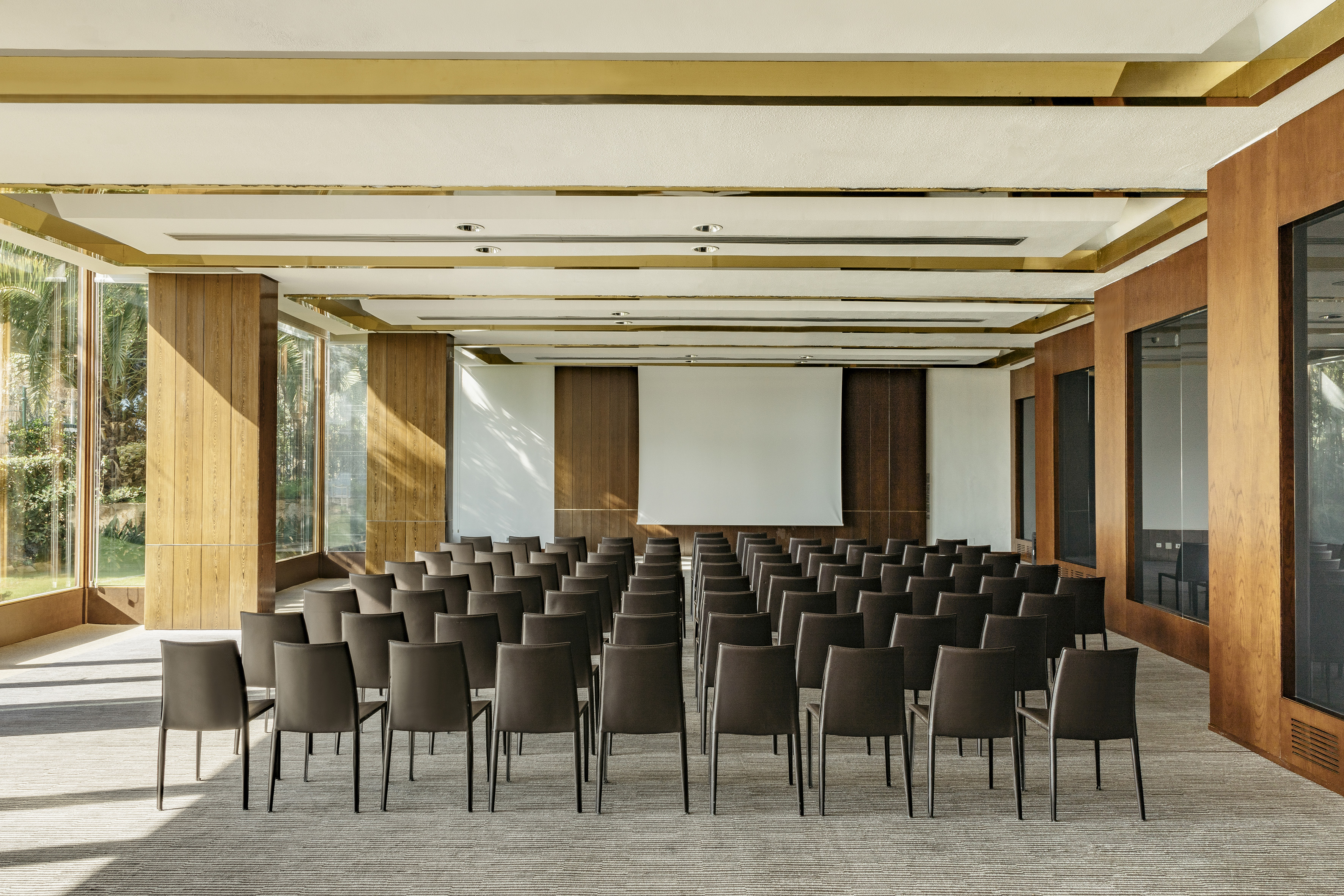Hotel conference room with empty chairs, white screen, and wood paneling.