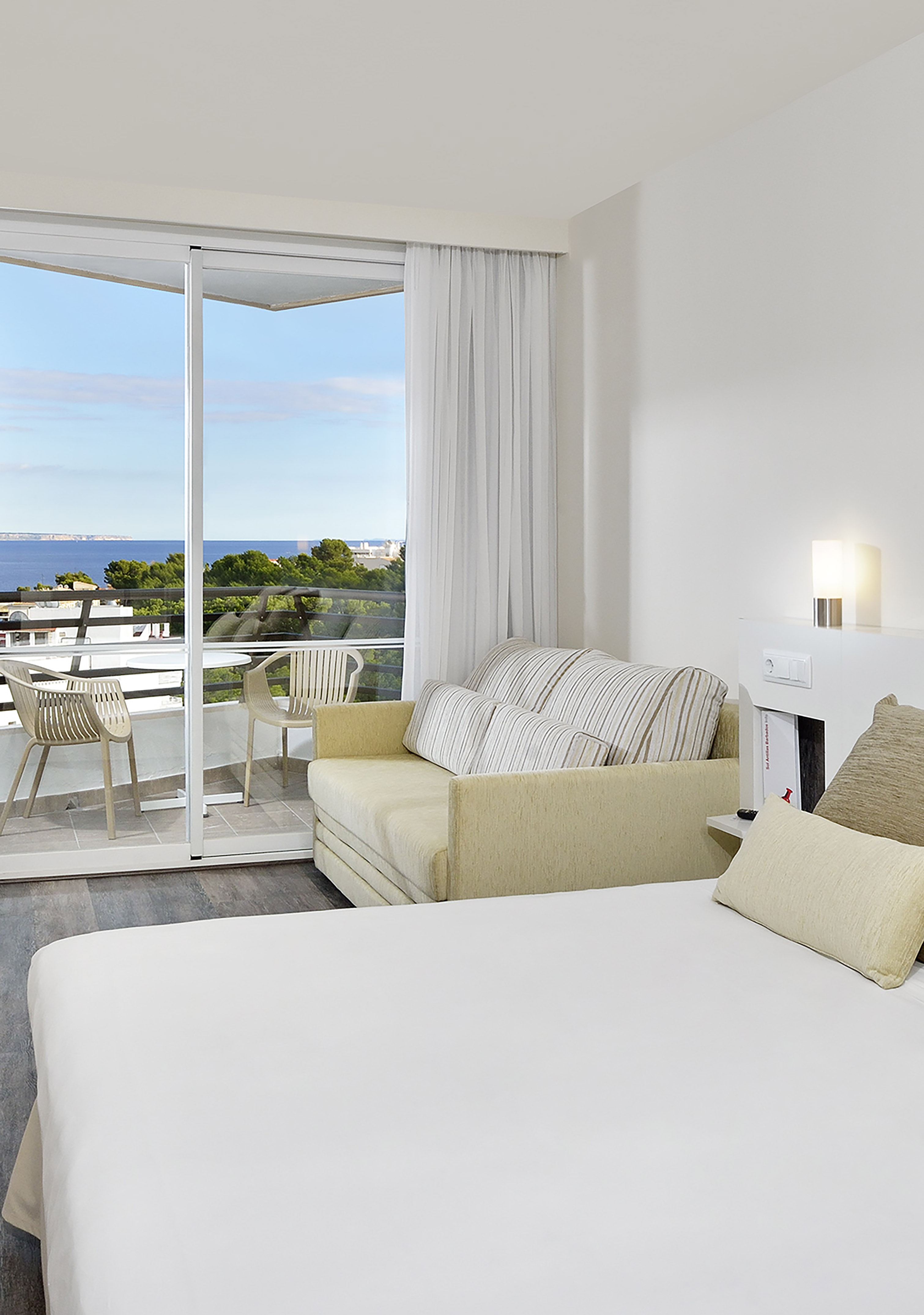 Modern hotel room with sea view balcony, bed, and sofa.