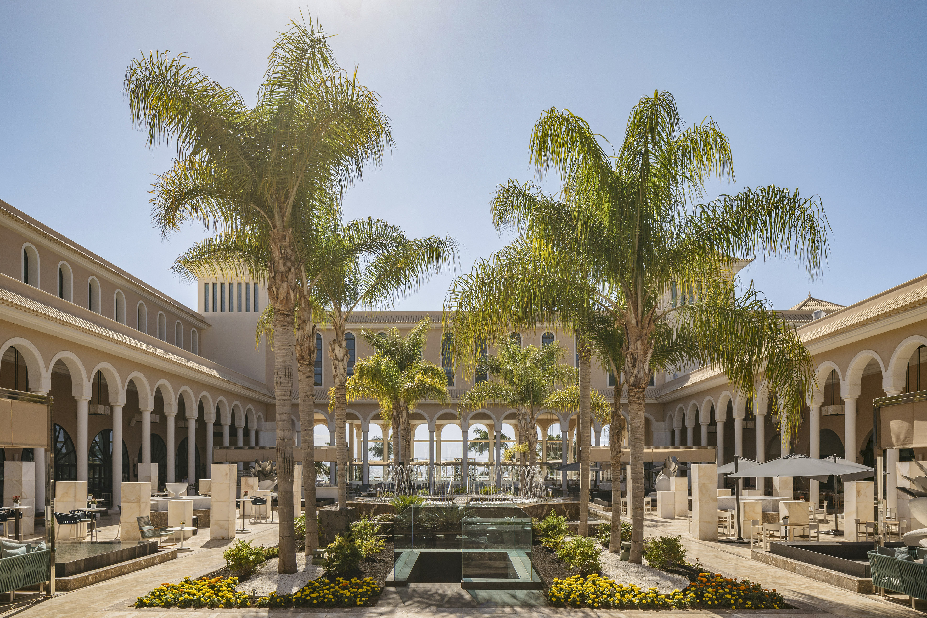 Luxury hotel courtyard with palm trees, fountain, and arched architecture.