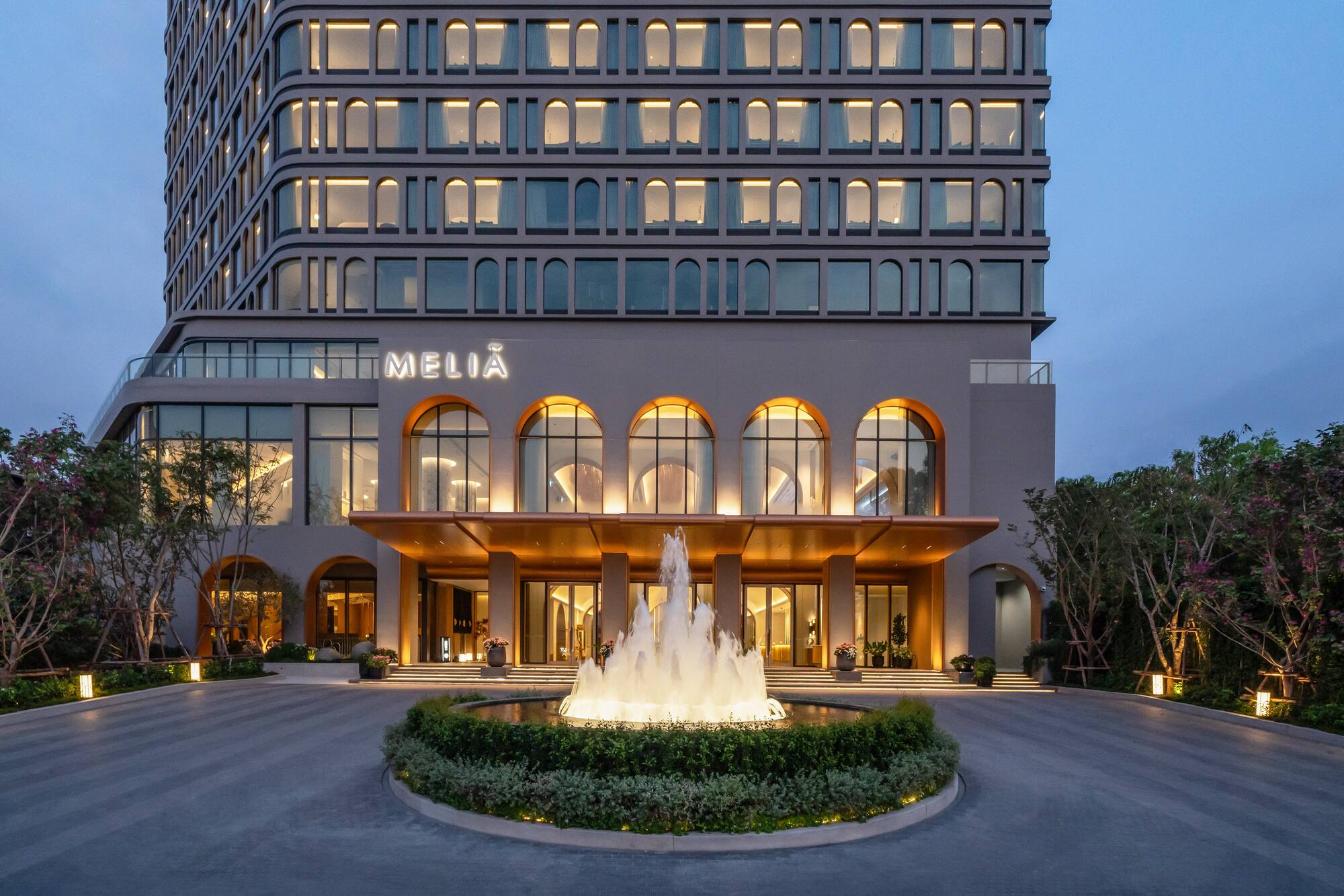 Melia hotel exterior at twilight with illuminated arched entrance and glowing fountain.