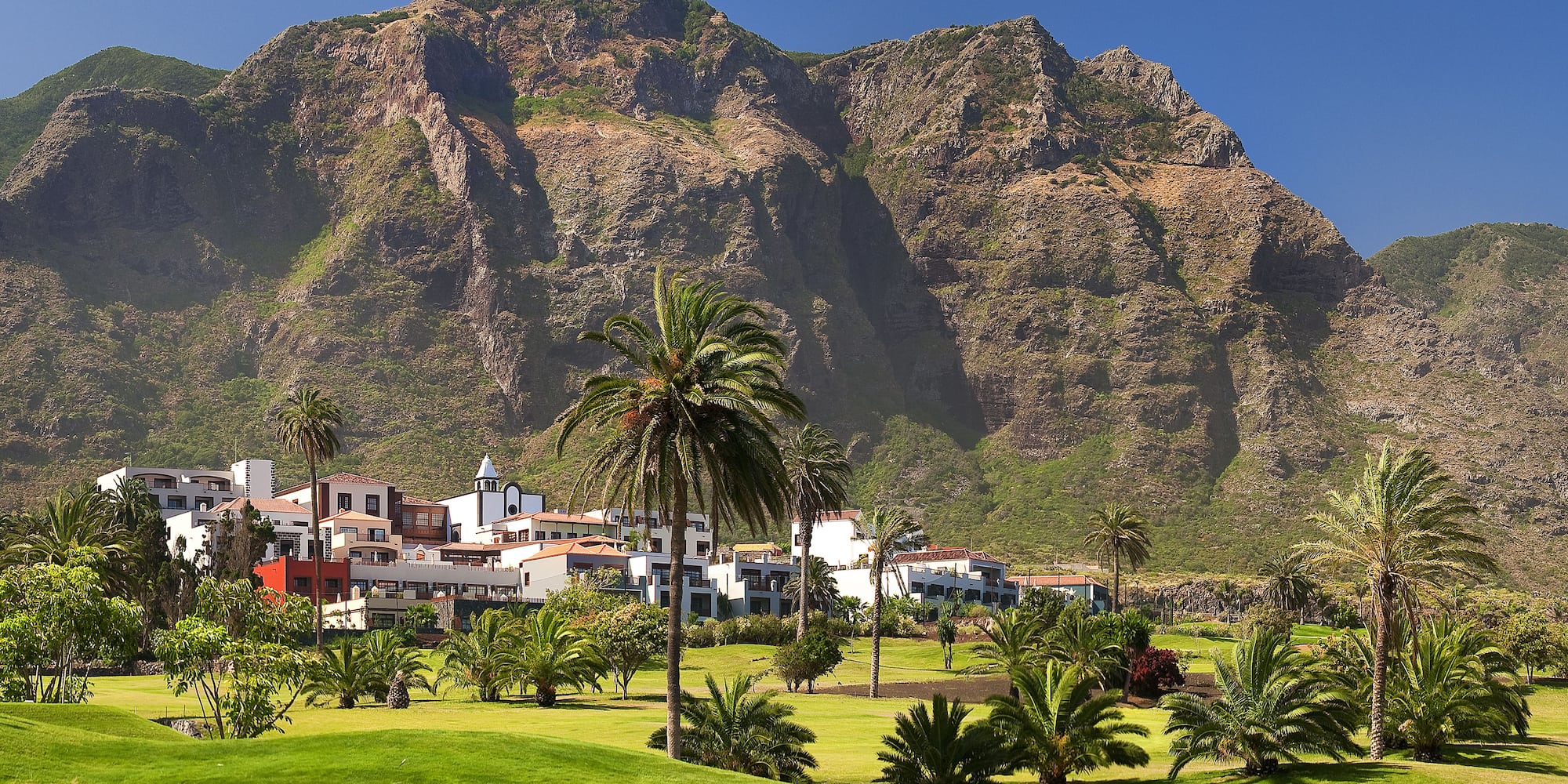 Lush golf course, resort buildings, palm trees, and steep mountains.