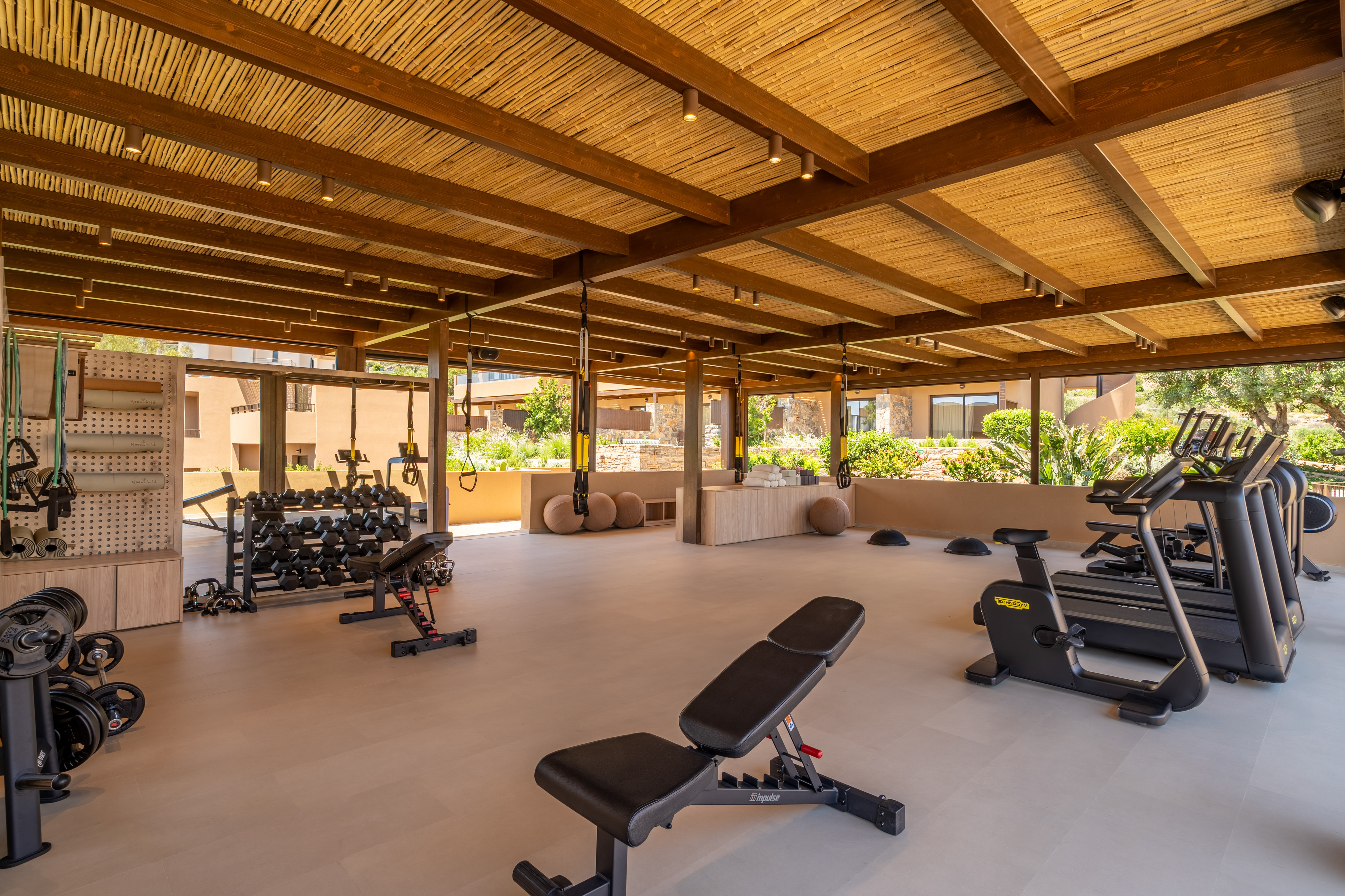 Open-air resort gym with cardio, free weights, and a bamboo ceiling.