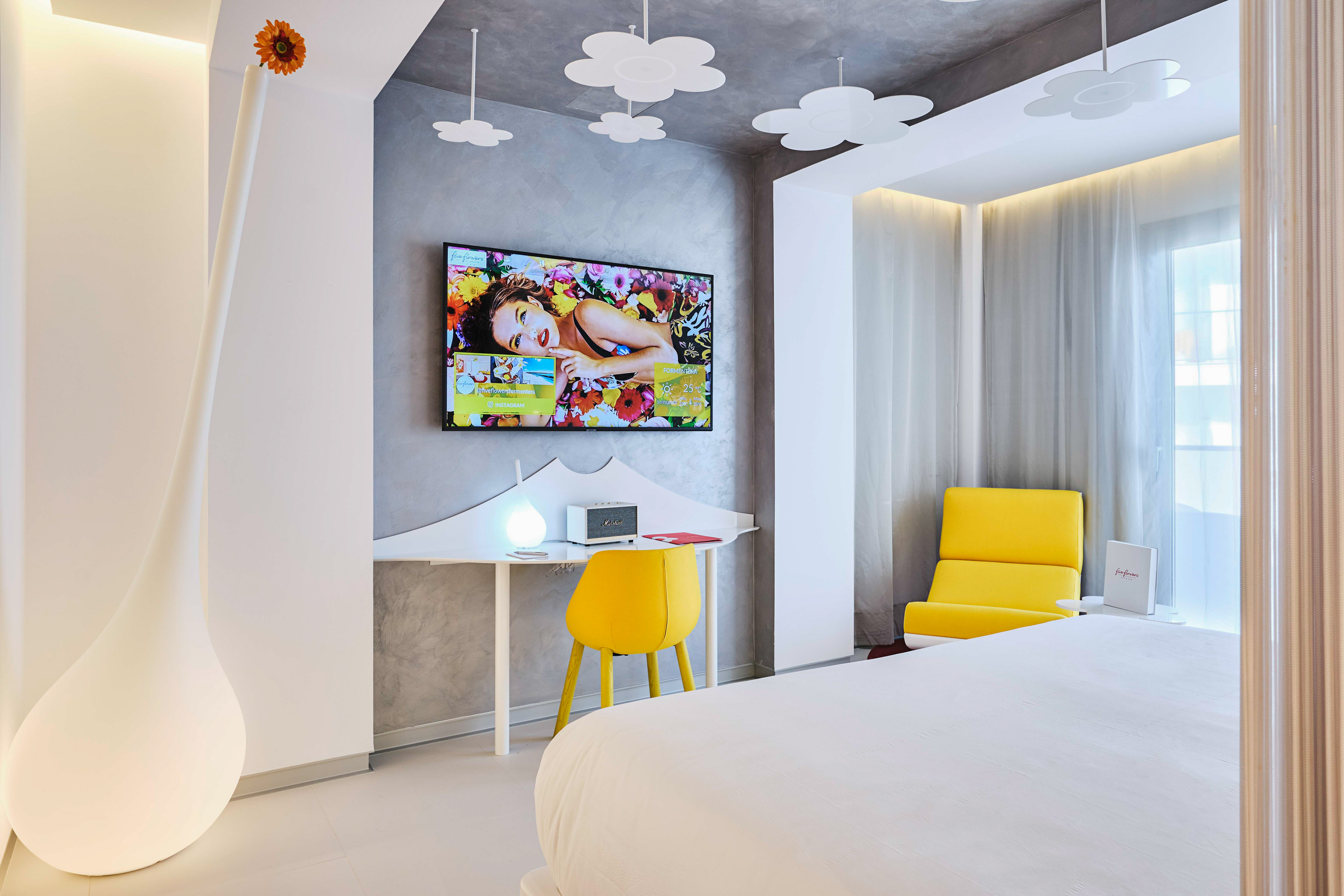 Modern hotel room with white bed, yellow accents, and flower ceiling lights.