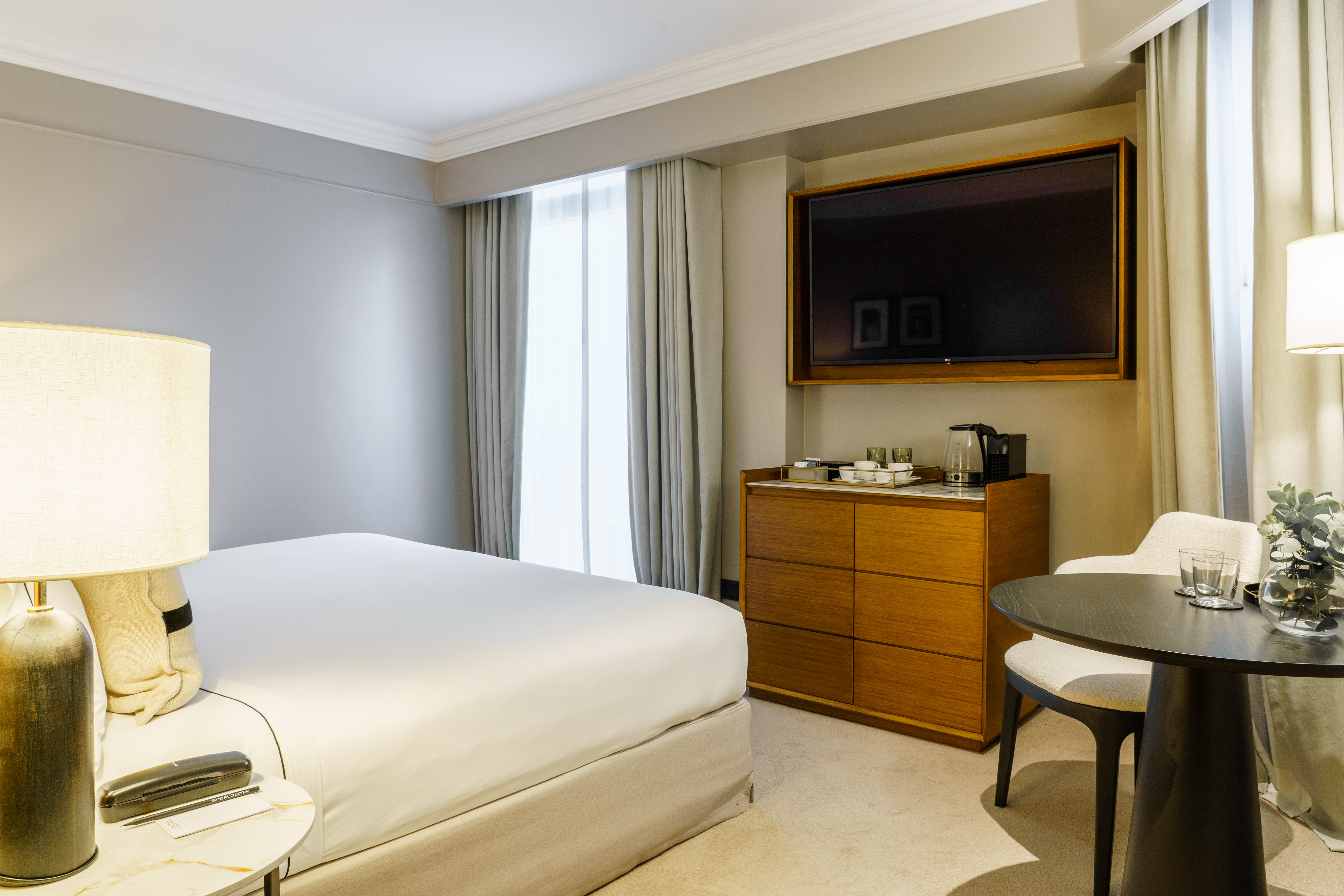 Luxury hotel guest room with bed, TV, wooden dresser, and round table.